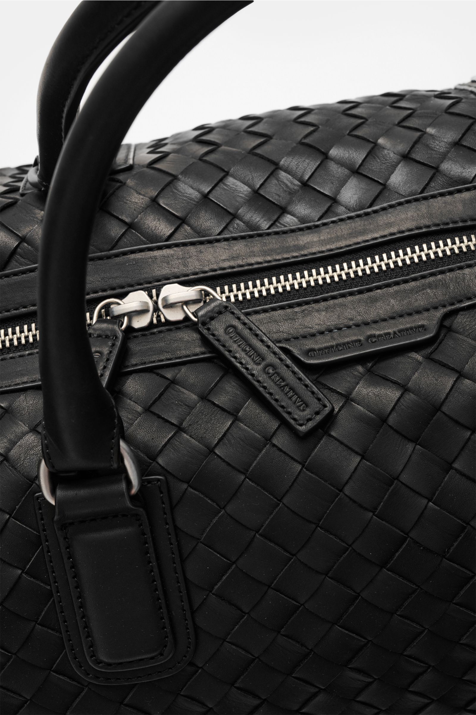 Nahaufnahme des fein genarbten, gewebten Leders und des robusten Zwei-Wege-Reißverschlusses des Officine Creative Weekender schwarz, fotografiert von schräg oben.