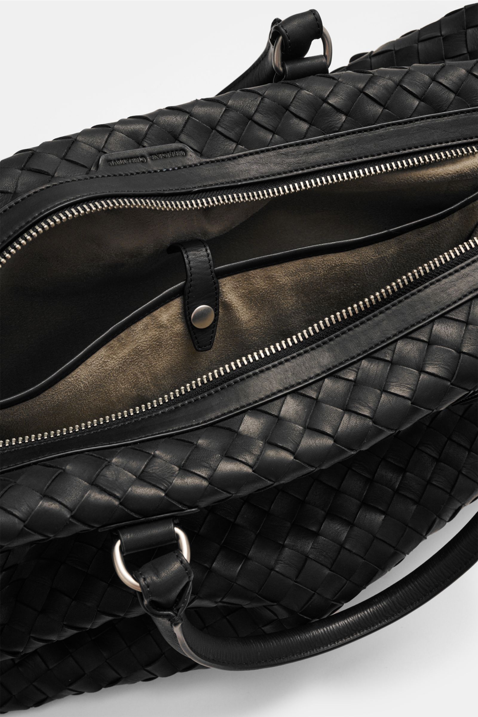 Officine Creative Weekender schwarz aus fein genarbtem, handgewebtem Leder mit silberner Hardware, offen von oben fotografiert.