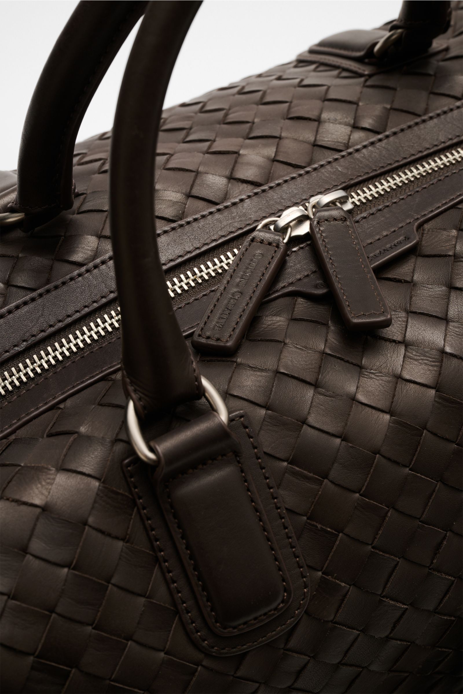 Officine Creative Weekender dunkelbraun aus fein genarbtem, gewebtem Leder mit matten, silberfarbenen Metall-Reißverschlüssen, Nahaufnahme von oben.