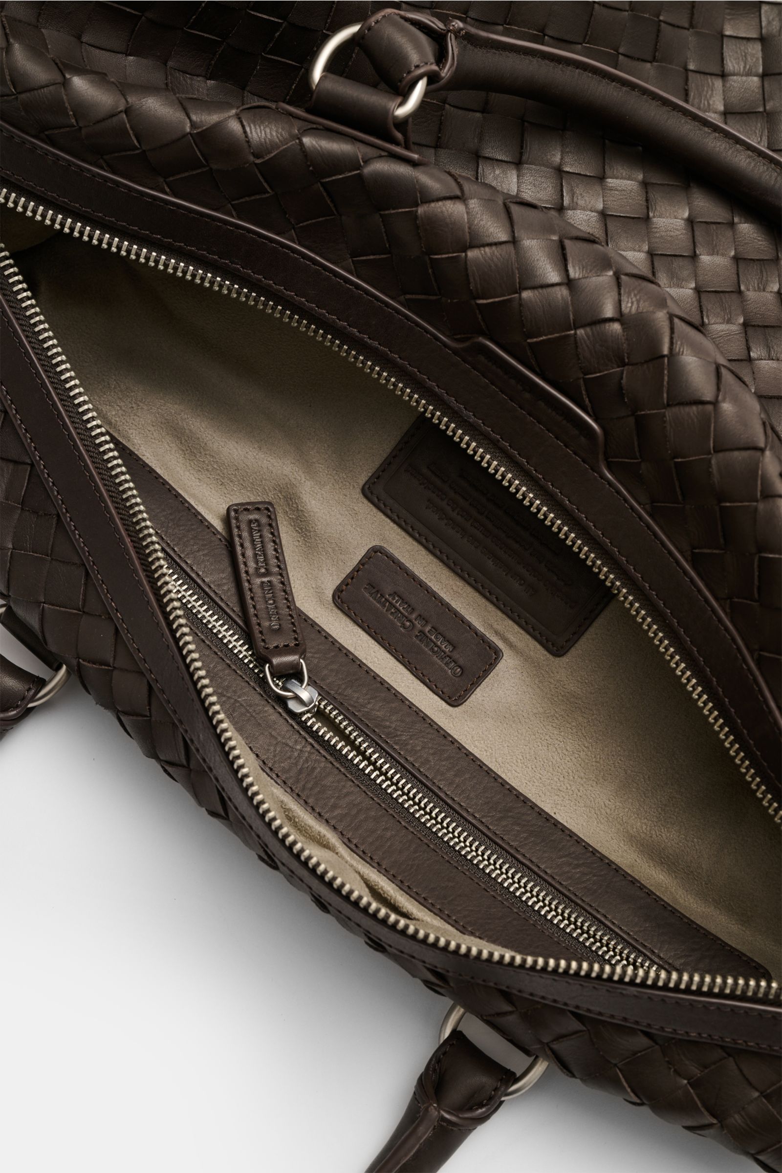 Officine Creative Weekender dunkelbraun aus handgewebtem Leder, geöffnet, Innenansicht mit Alcantara-Futter und Zipperfach, matte silberne Hardware.