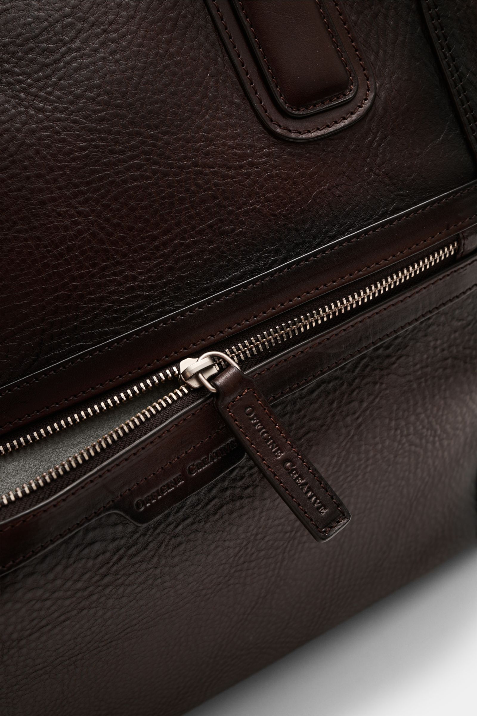 Officine Creative Weekender dunkelbraun aus fein genarbtem Leder mit matter Hardware, Zipper-Außenfach und robusten Tragegriffen, Nahaufnahme seitlich.