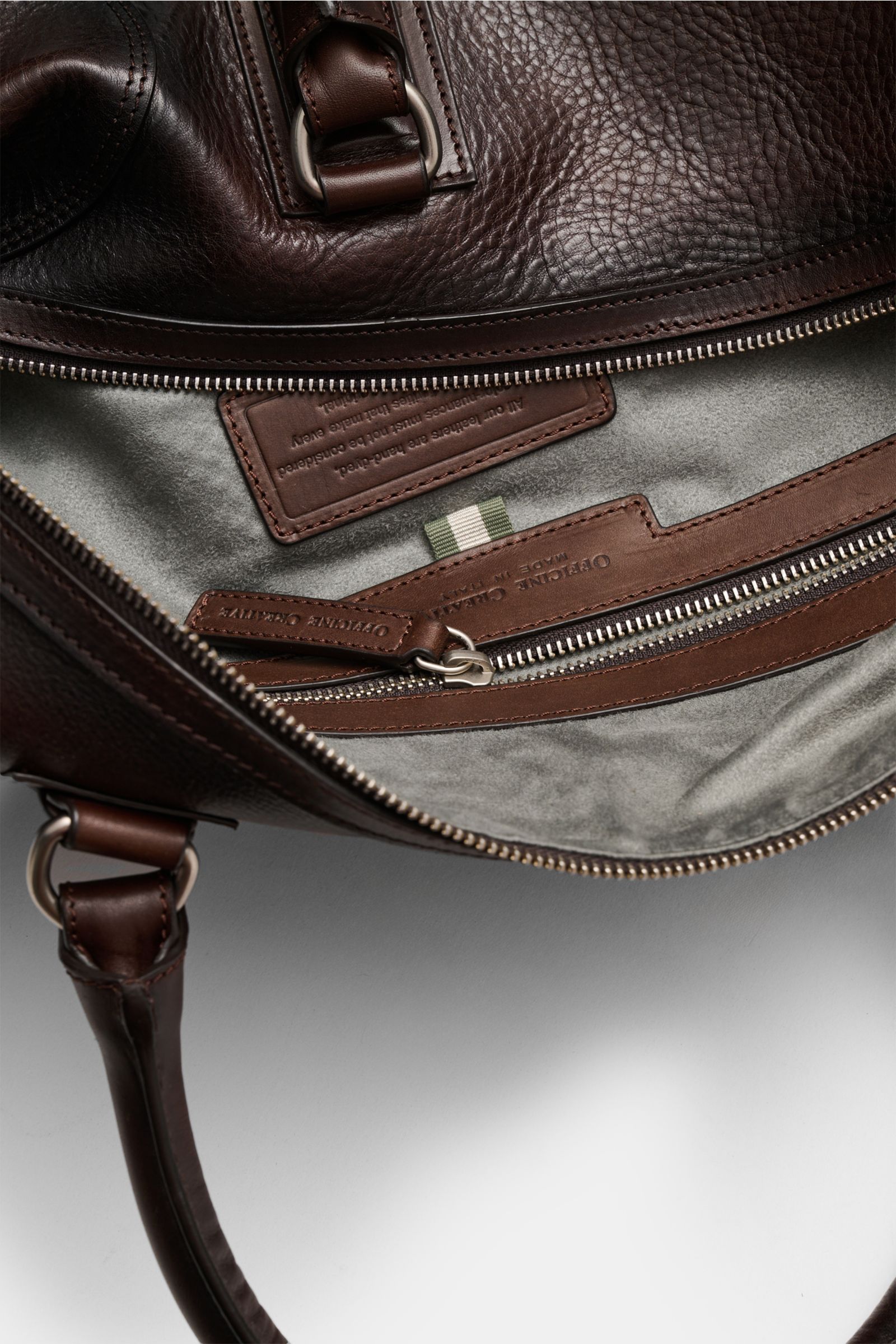 Officine Creative Weekender dunkelbraun aus fein genarbtem Leder, geöffnet von oben, mit silberner Hardware, Zipperfach und Alcantara-Futter.