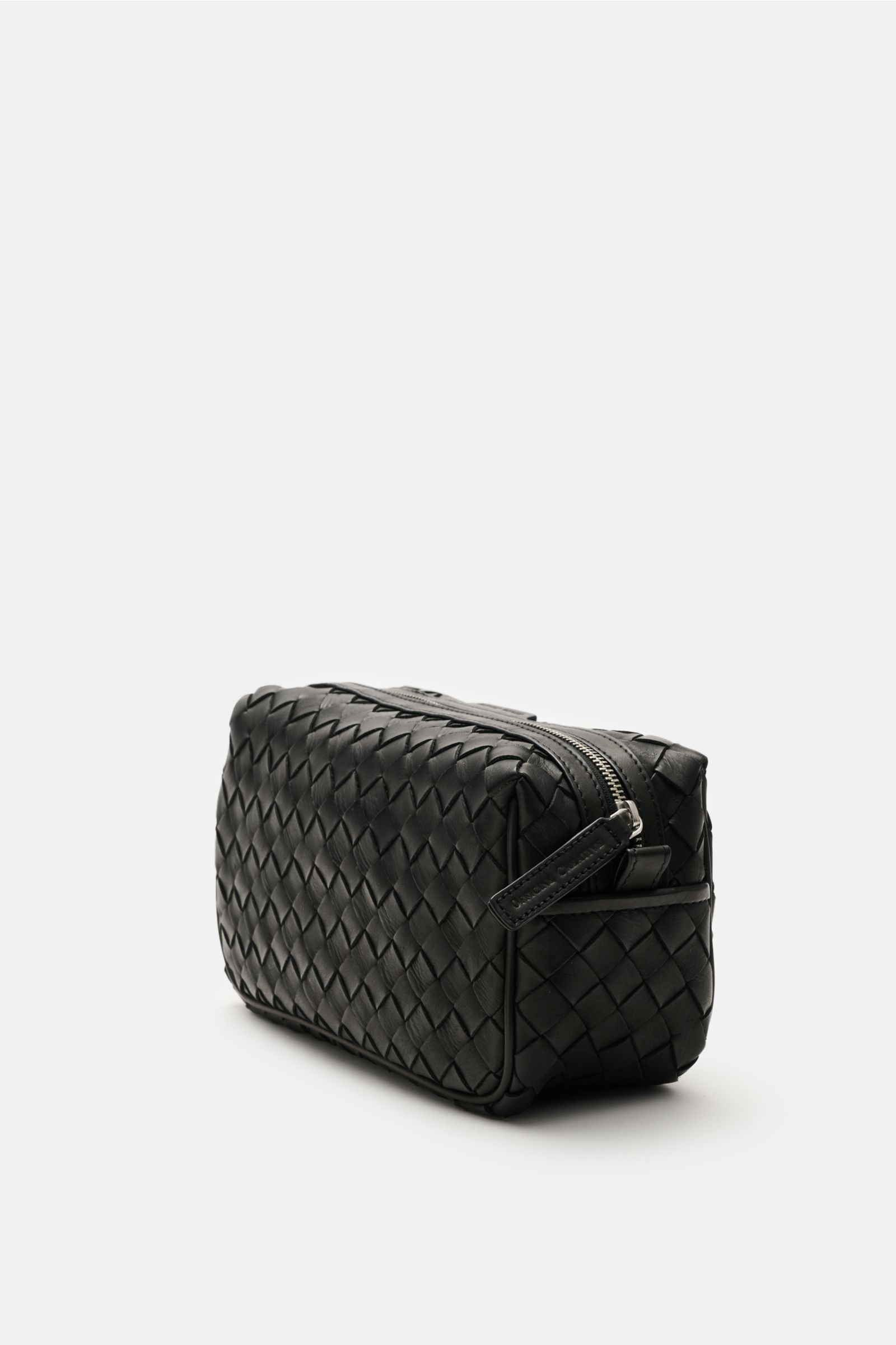 Officine Creative Necessaire schwarz shown from a side angle, with black braided leather exterior, silver hardware, zippered outer pocket, spacious main compartment, practical wrist strap, measuring approx. 25x15x10 cm; practical travel essential perfect 