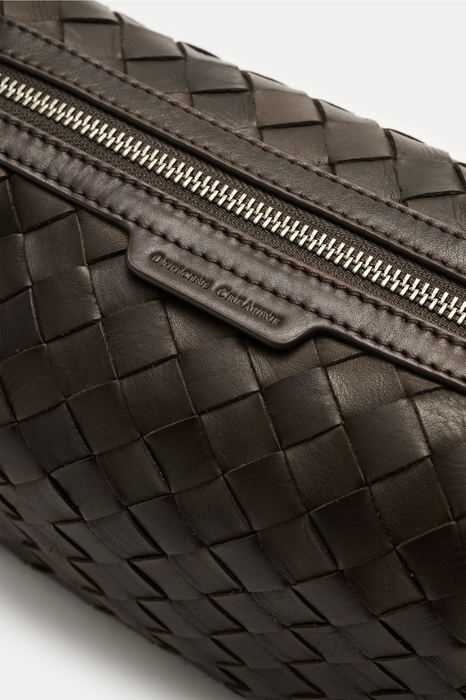 Nahaufnahme des Officine Creative Necessaire dunkelbraun mit geflochtener Leder-Außenseite und silberfarbenem Reißverschluss.