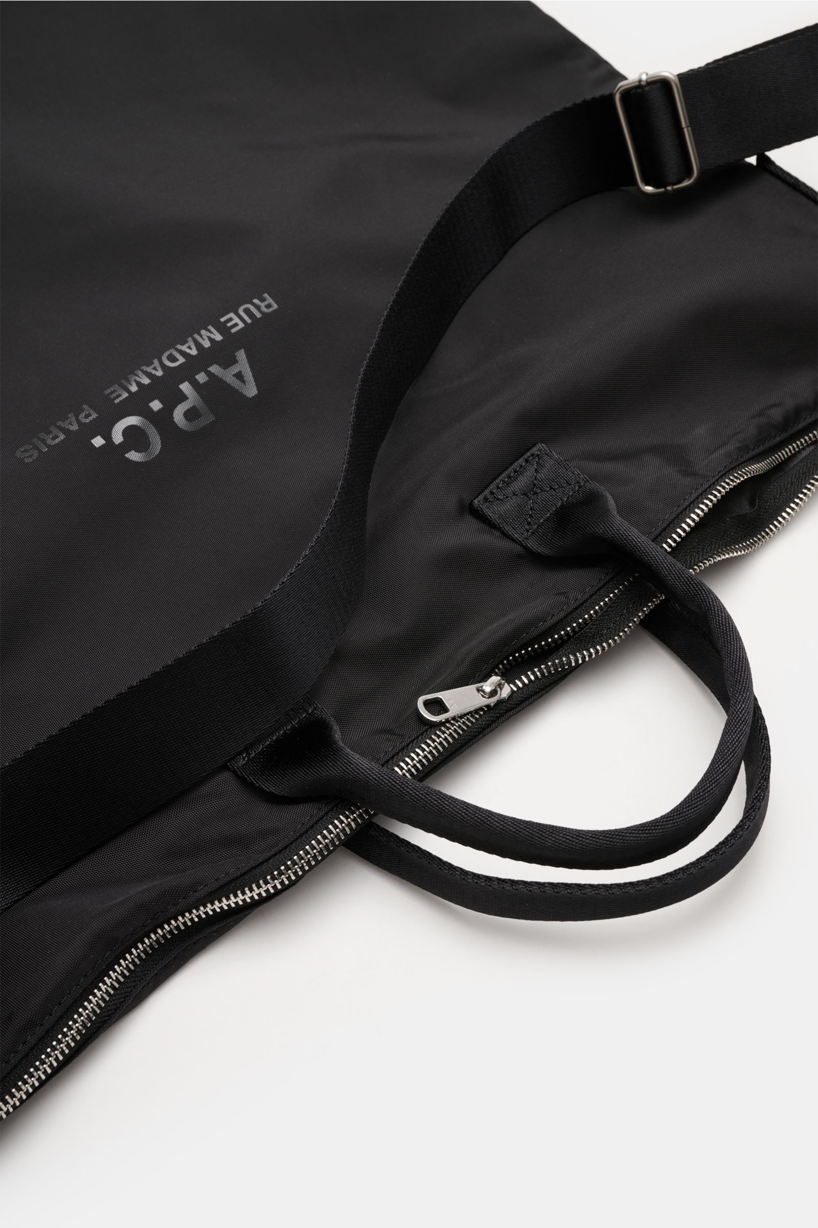 Black A.P.C. Tasche 'Crossbody Bag Backstage' schwarz photographed from a top angle, showing silver zipper, textile handles, adjustable strap, and front logo print. Versatile everyday companion made of high-quality microfiber with spacious main compartmen