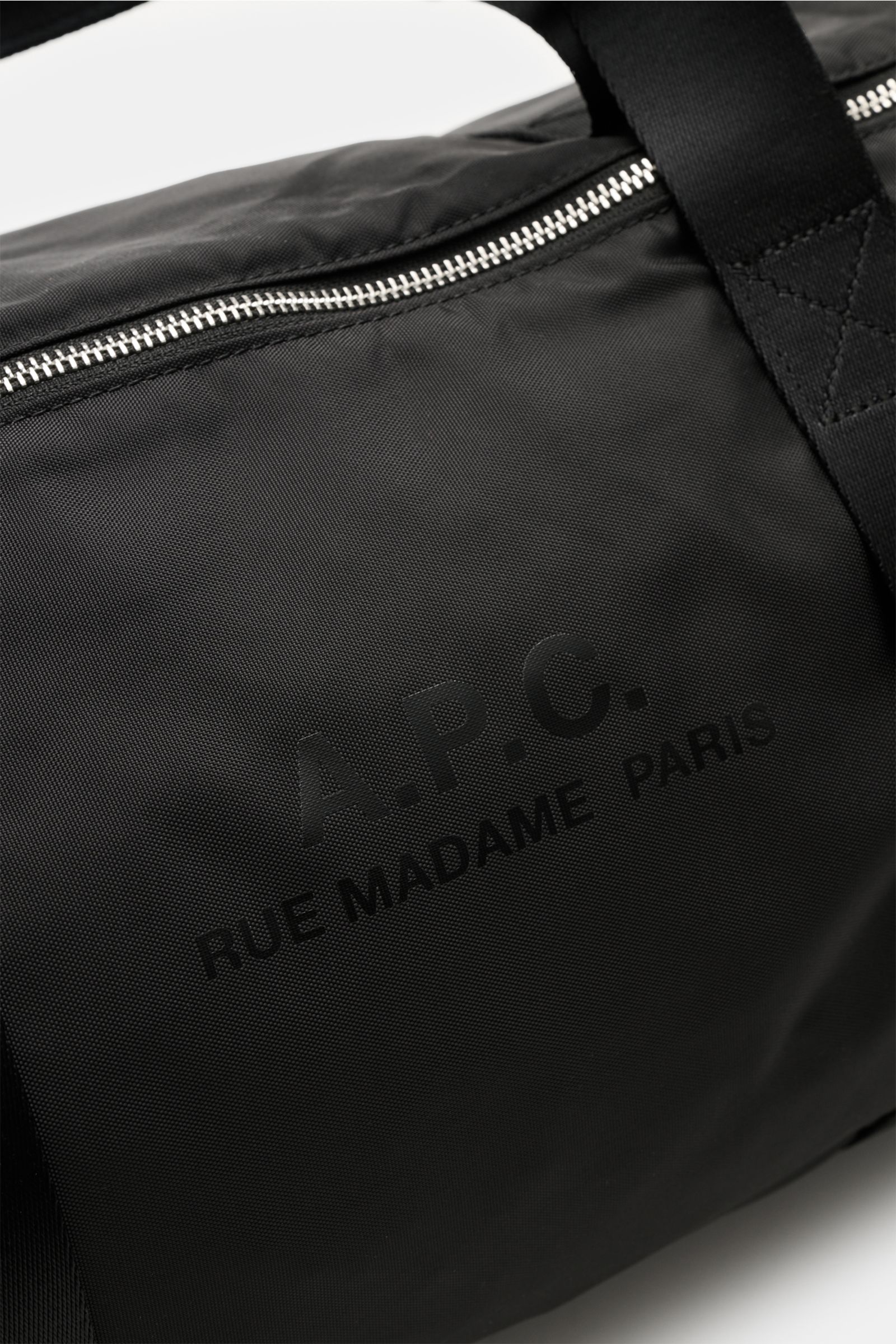 Close-up front-side view of the black A.P.C. Tasche 'Gymbag Backstage' schwarz showing silver zipper, durable textile straps, and subtle logo print on high-quality microfiber. Ideal for training and everyday use, featuring a spacious main compartment, zip
