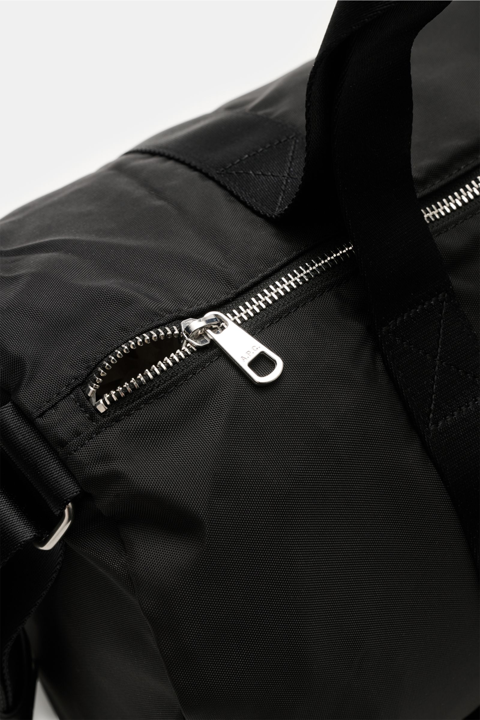 Close-up view of A.P.C. Tasche 'Gymbag Backstage' schwarz black gym bag showing silver zipper and durable textile straps.

This image features the A.P.C. Tasche 'Gymbag Backstage' schwarz, an ideal companion for training and everyday use with a clean desi