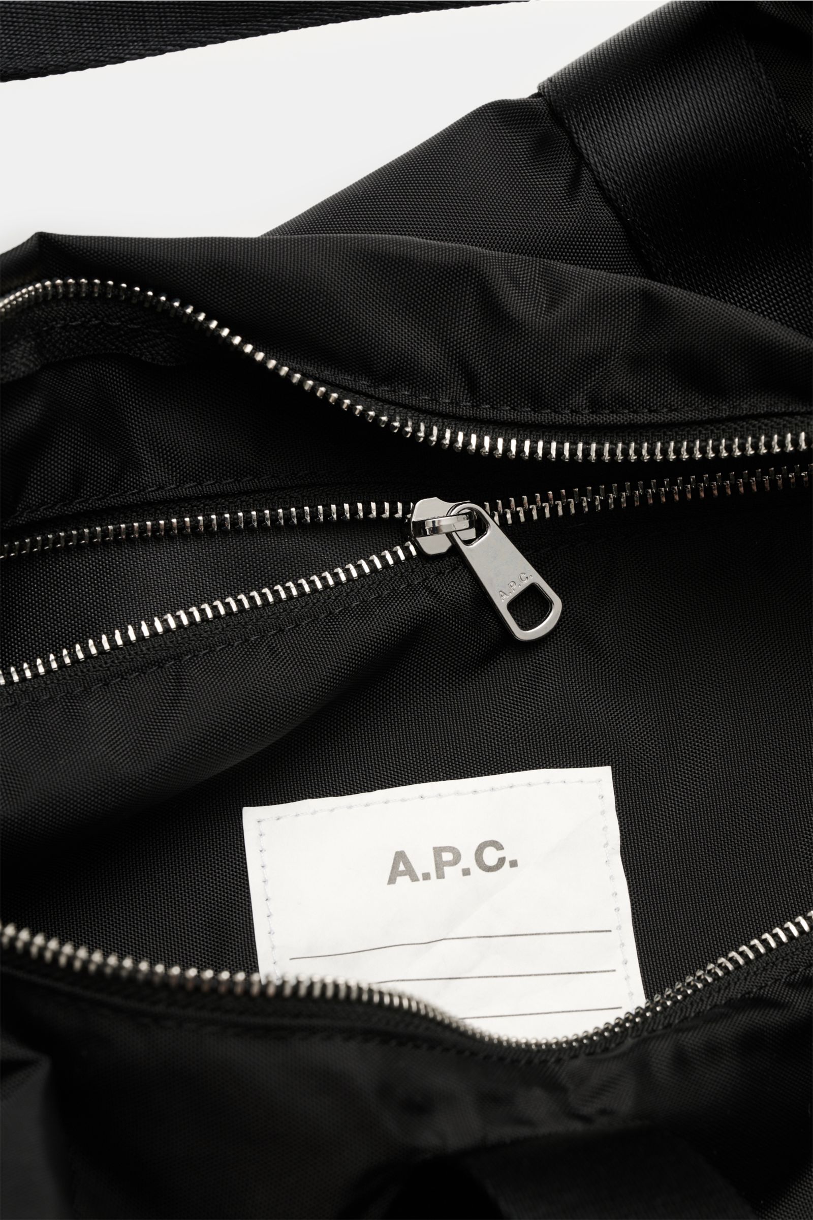 Close-up inside view of A.P.C. Tasche 'Gymbag Backstage' schwarz showing silver zipper, black microfiber fabric, and white logo label.

The A.P.C. Tasche 'Gymbag Backstage' schwarz is an ideal companion for training and everyday use, featuring high-qualit