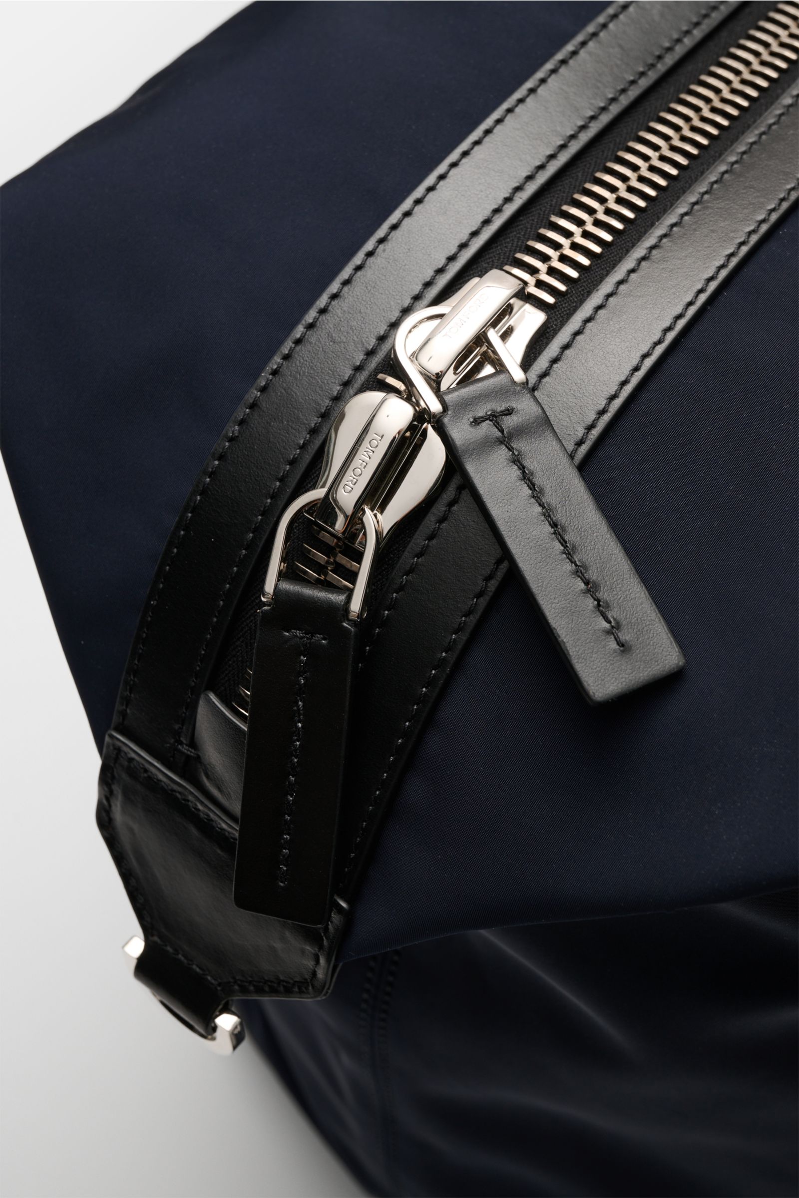 Close-up detail of the Tom Ford Weekender navy/schwarz showing the oversized silver zipper and black leather trim from a top-side perspective.

Description: Mit diesem Weekender aus robuster Microfaser und edlem Kalbleder von TOM FORD sind Sie perfekt 