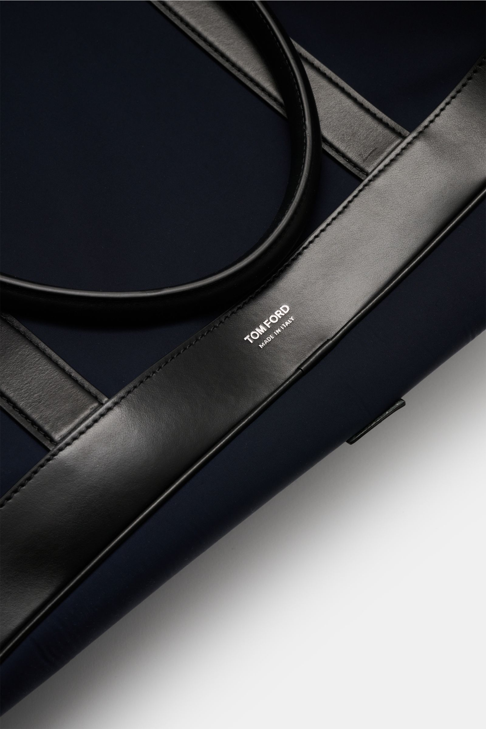 Close-up top view of Tom Ford Weekender navy/schwarz with black calf leather handles and logo on navy microfiber body.

Description: Mit diesem Weekender aus robuster Microfaser und edlem Kalbleder von TOM FORD sind Sie perfekt vorbereitet auf den näch