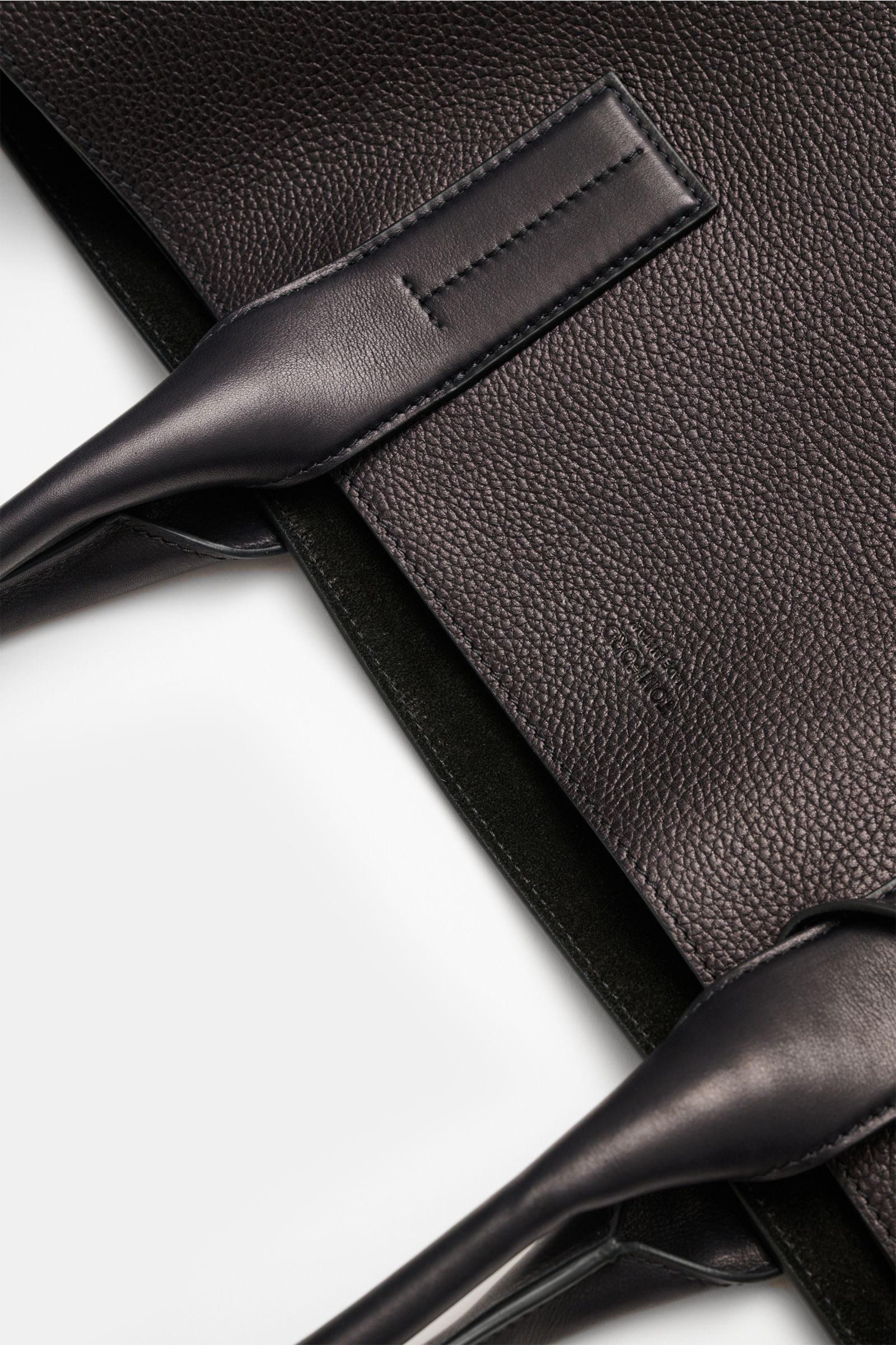 Close-up top-down view of the Tom Ford Shopper schwarz showing finely grained calf leather, smooth leather handles, silver hardware, and subtle logo embossing.

Ob im Office oder unterwegs in der City: Dieser luxuriöse Shopper von TOM FORD aus genarbte