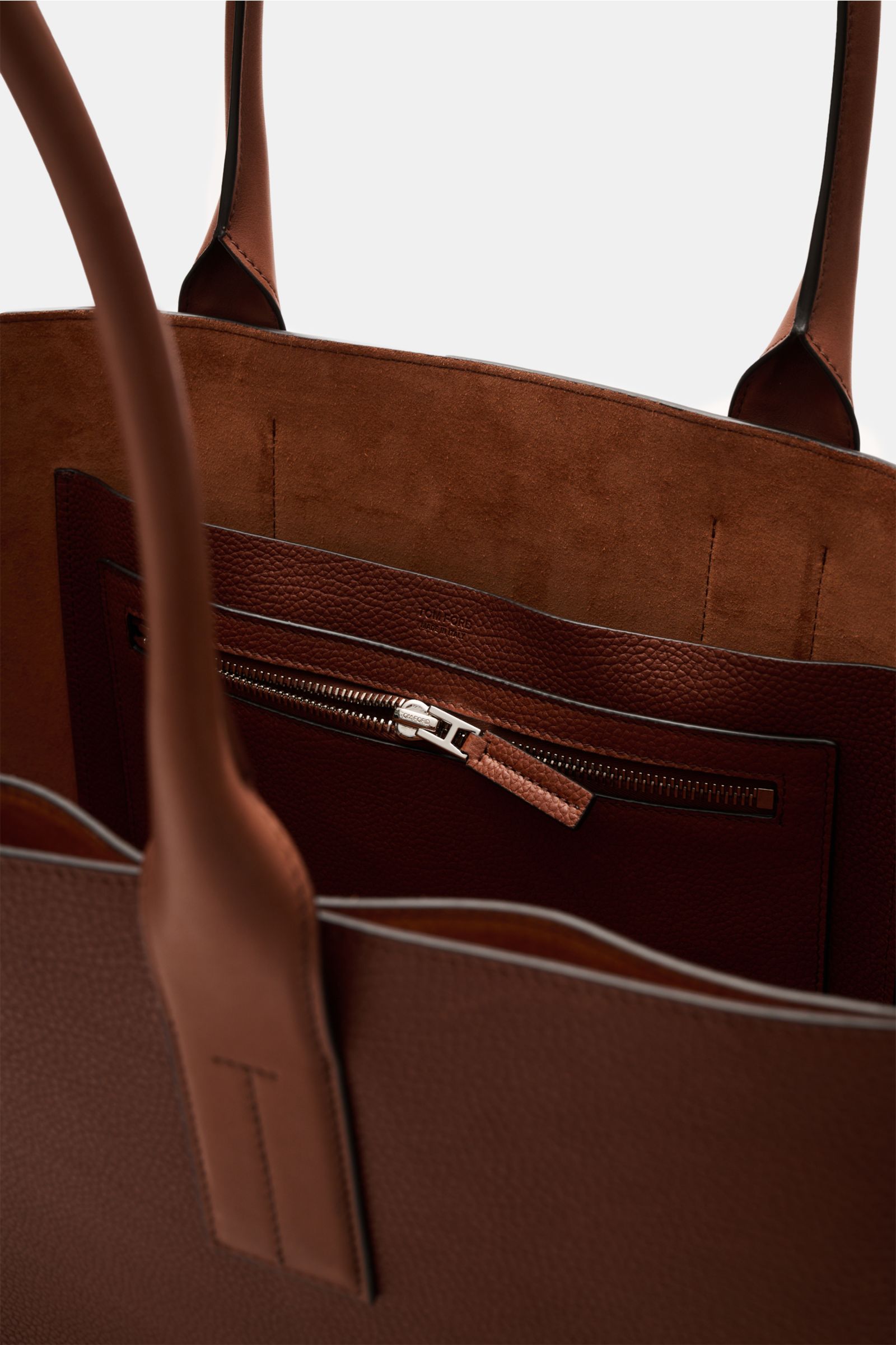 Close-up interior view of the Tom Ford Shopper rotbraun in finely grained calf leather with smooth leather details, silver hardware, spacious main compartment, zippered pocket, two slip pockets, suede lining, and subtle front logo embossing.