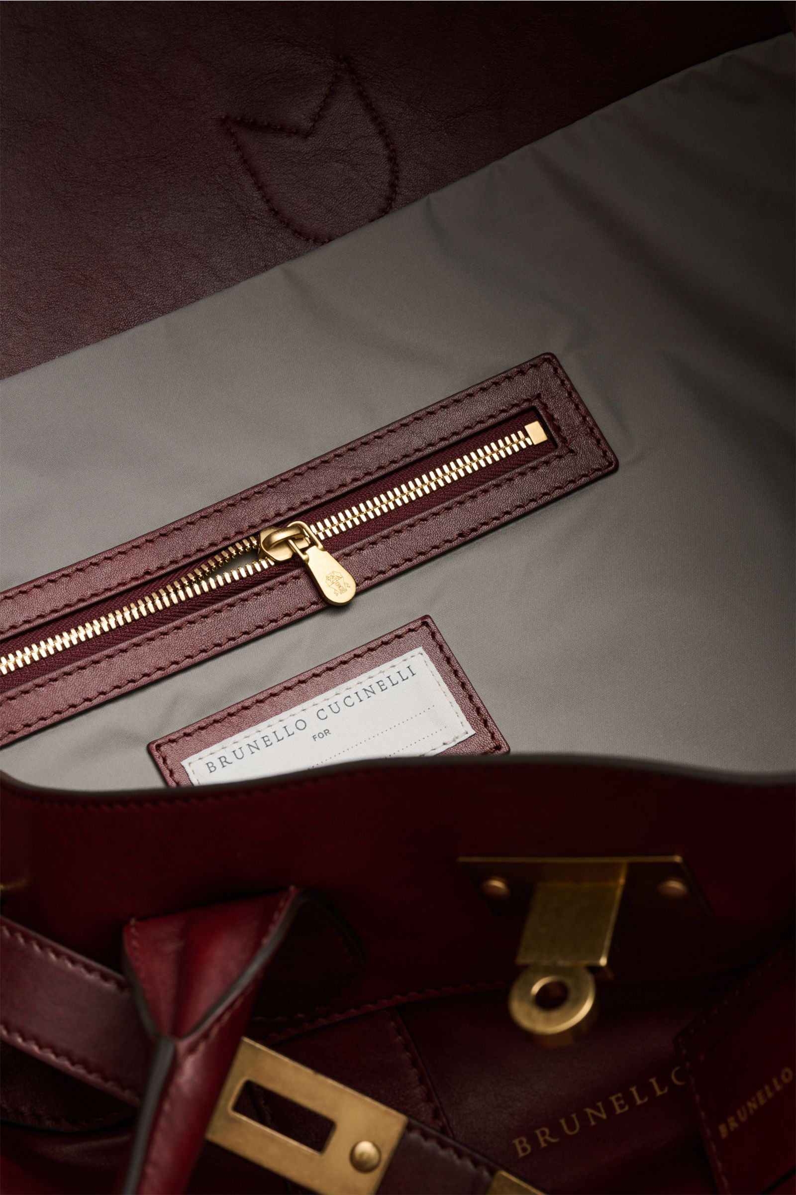 Innenansicht des Brunello Cucinelli Weekender bordeaux aus genarbtem Kalbsleder mit goldfarbener Hardware, Reißverschlussfach, verstellbarer Lederschließe und wasserabweisendem Innenfutter.