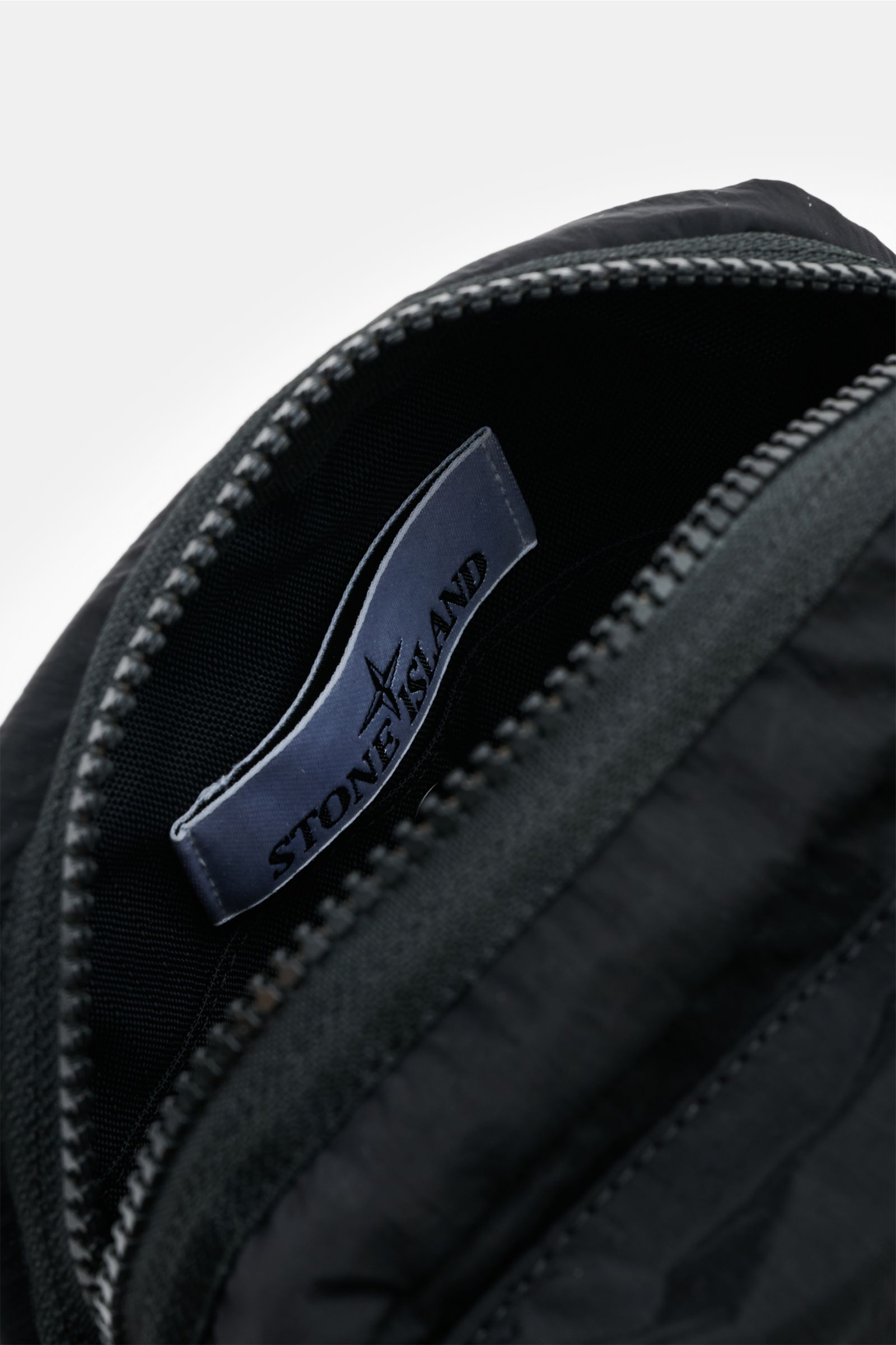 Close-up view inside the Stone Island Crossbody Bag 'Marsupio Tracolla' schwarz showing the STONE ISLAND label and zipper.

Description: Praktisch und stylish zugleich: Die Crossbody Bag 'Marsupio Tracolla' von STONE ISLAND überzeugt mit mehreren Fäche