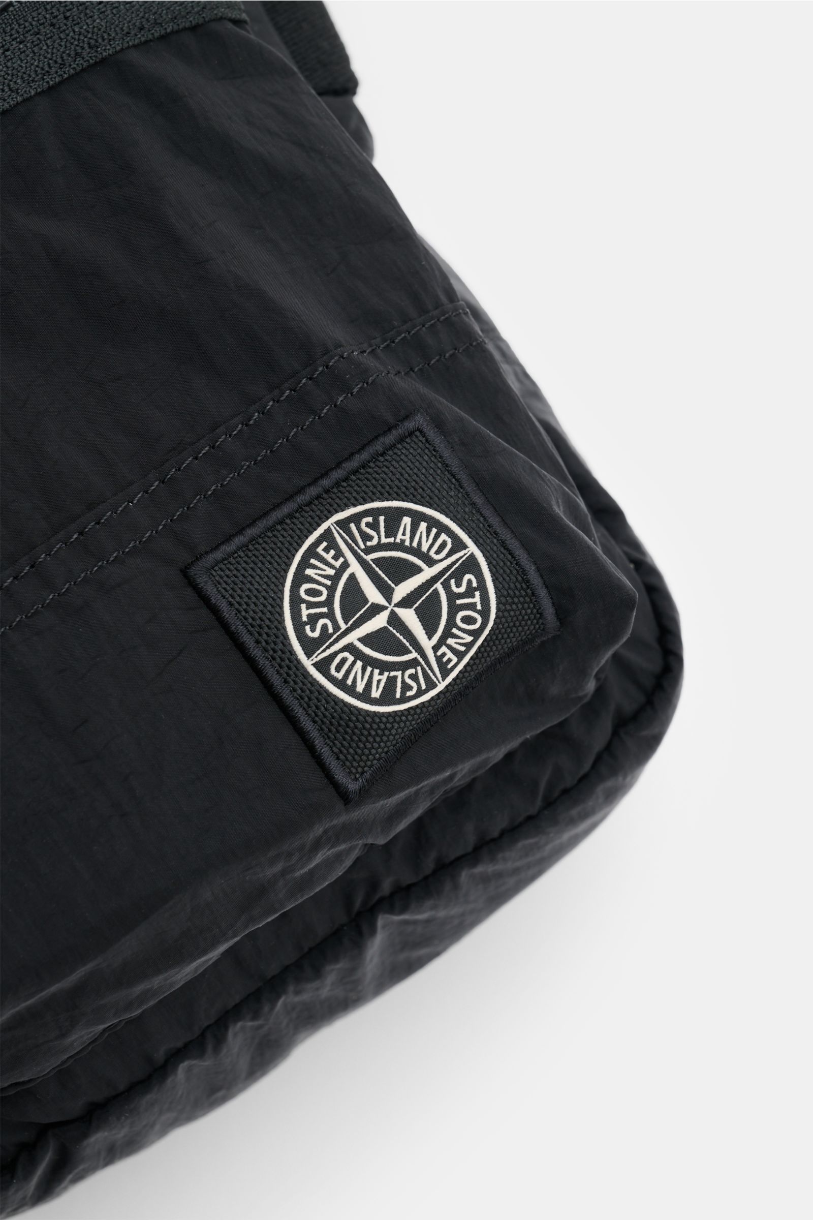 Close-up, angled view of the Stone Island Crossbody Bag 'Marsupio Tracolla' schwarz showing the black microfiber fabric and the distinctive Stone Island patch. 

Praktisch und stylish zugleich: Die Crossbody Bag 'Marsupio Tracolla' von STONE ISLAND übe