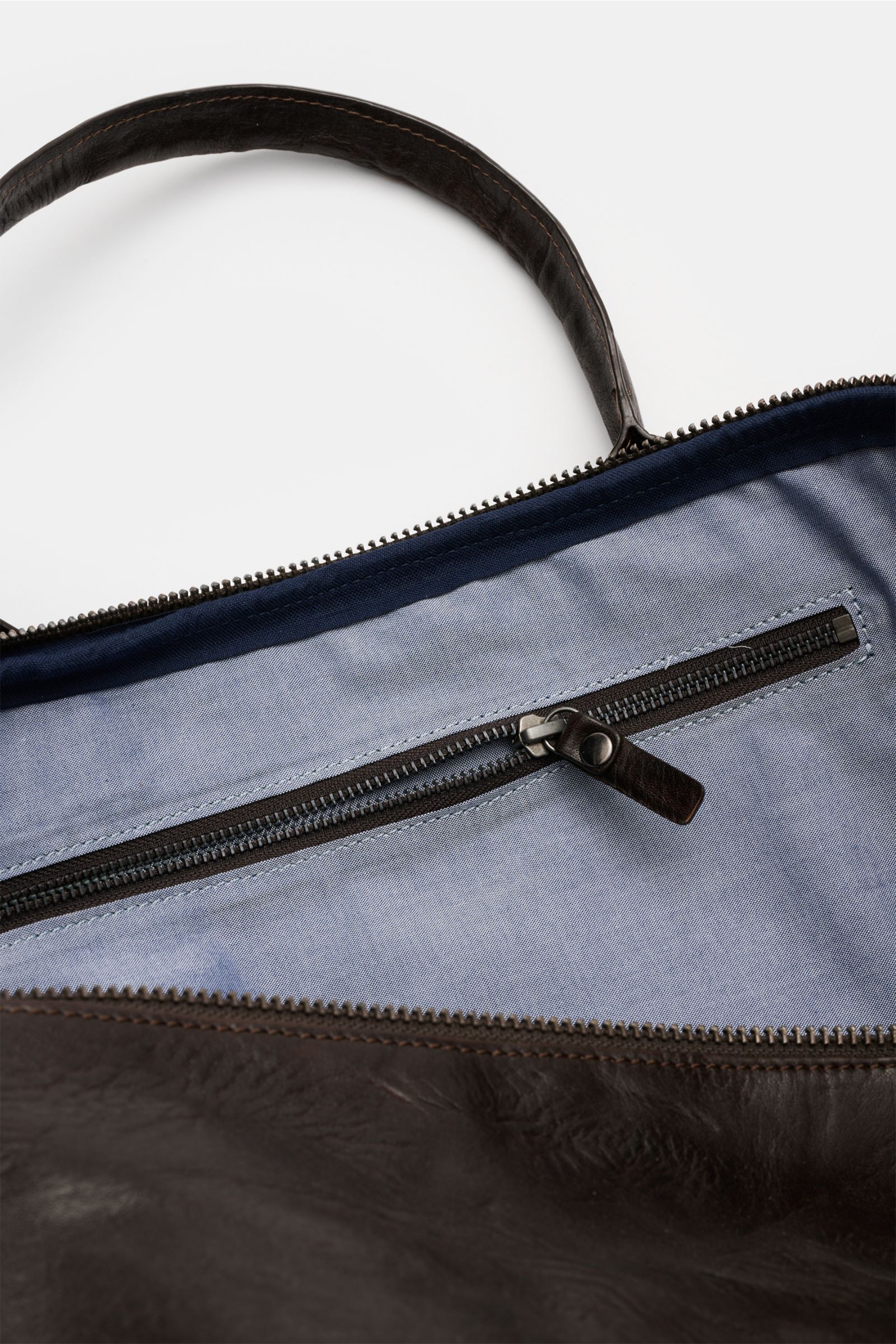 Close-up top-down view of the inside of the 04651/ A trip in a bag Weekender '356-Bag Crushed' dark brown, showing the light blue textile lining and internal zip compartment. When holiday time comes, you won’t want to be without the weekender '356-Bag Cru