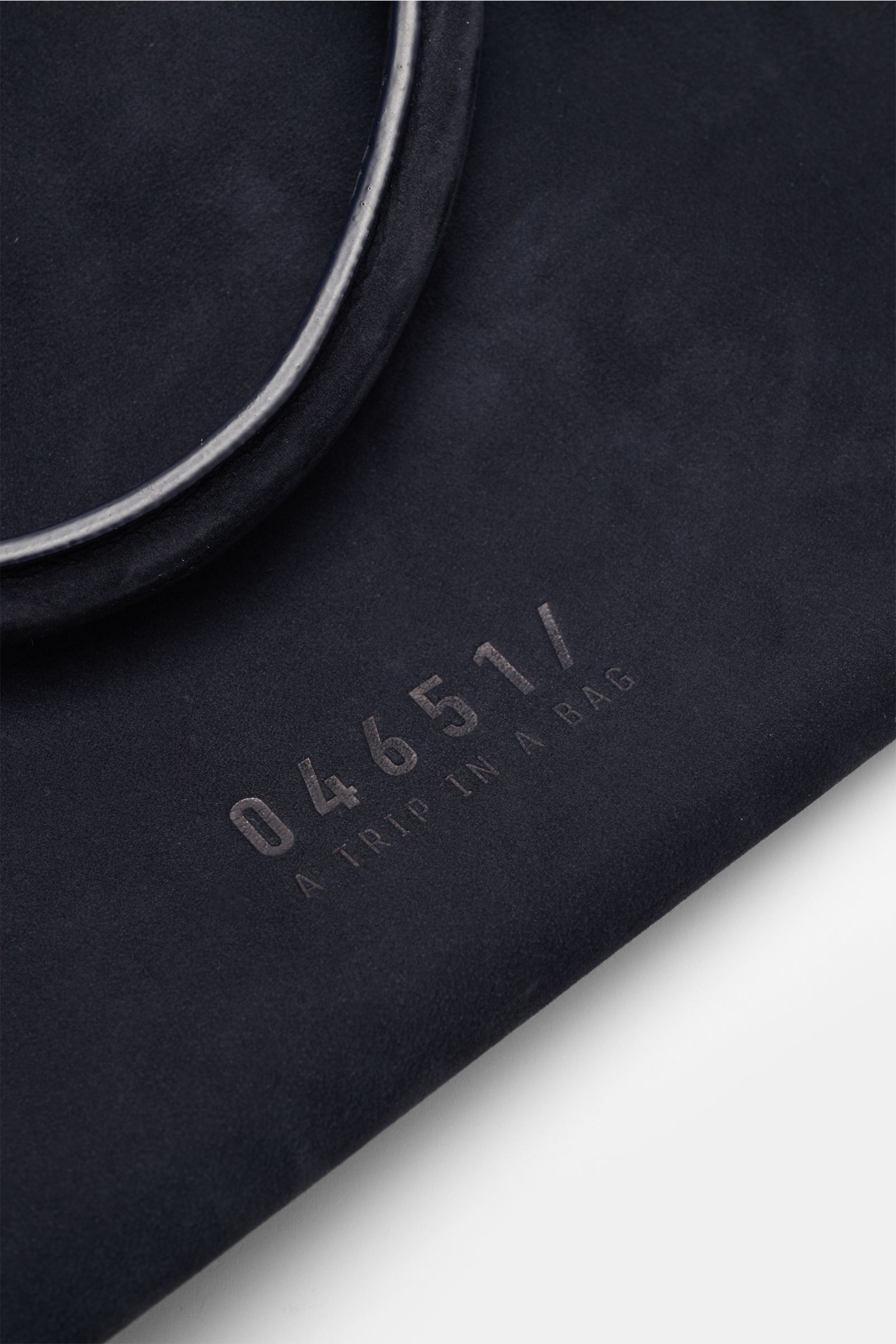 Close-up view of the navy velours leather surface and silver hardware of the 04651/ A trip in a bag Weekender '356 Bag' navy, showing soft texture and embossed logo from a top angle. The Weekender '356 Bag' from 04651/ A TRIP IN A BAG features smooth velo