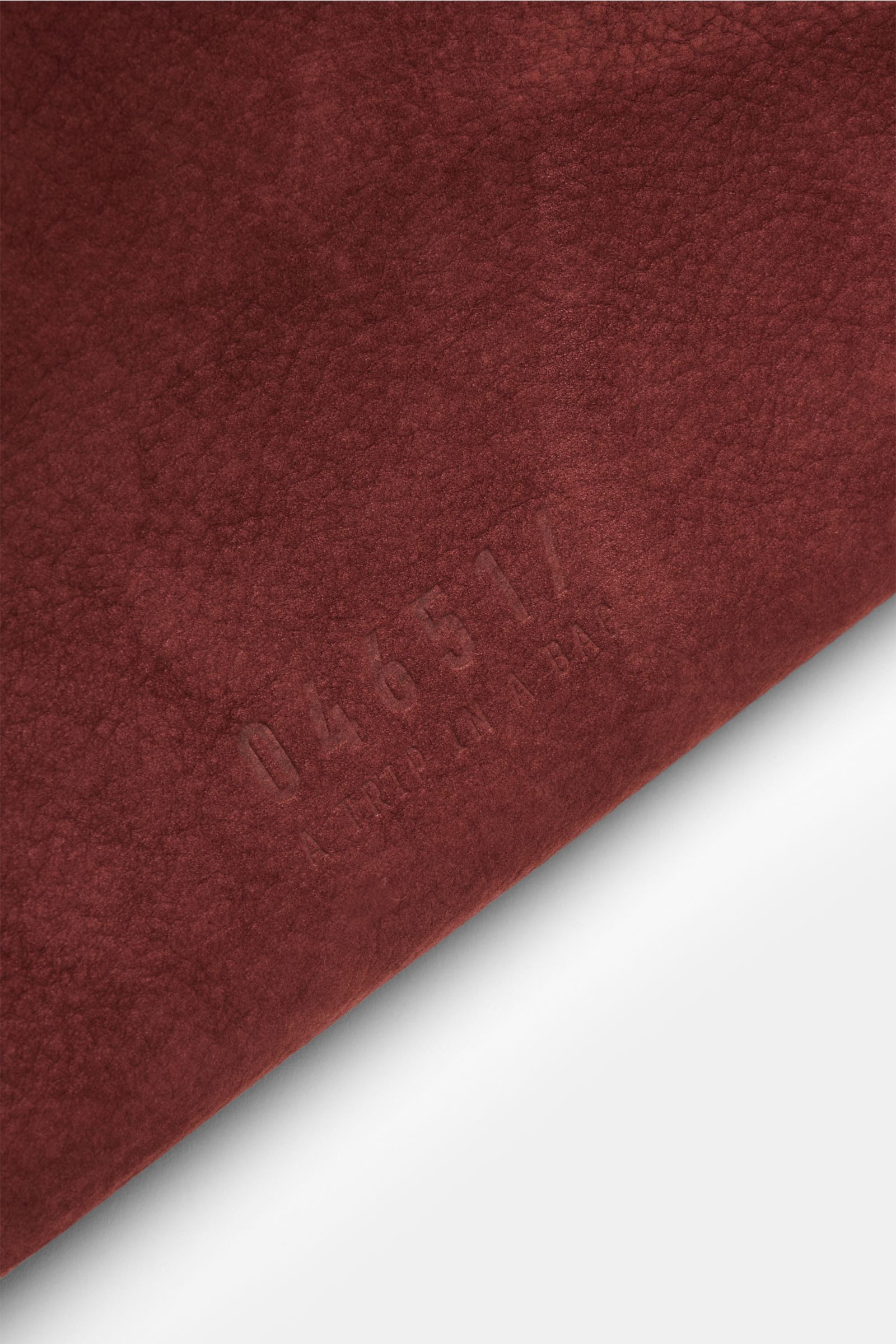 Close-up of the embossed logo on the red-brown velour leather surface of the 04651/ A trip in a bag Weekender '356 Bag,' photographed from an angled top view; Der Weekender '356 Bag' aus edlem Veloursleder von 04651/ A TRIP IN A BAG weicht Ihnen auf Ihren