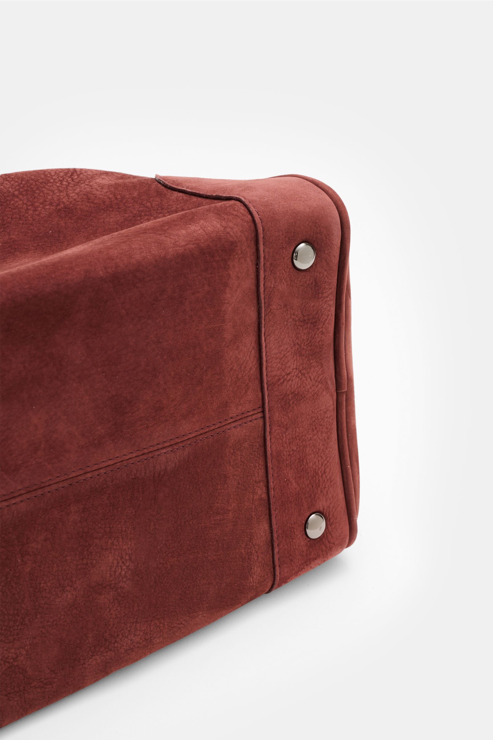 Close-up side view of the bottom corner of the 04651/ A trip in a bag Weekender '356 Bag' rotbraun, showing soft velours leather, metal feet, and detailed stitching. The bag features smooth velours leather in rotbraun, silver-colored hardware, robust hand