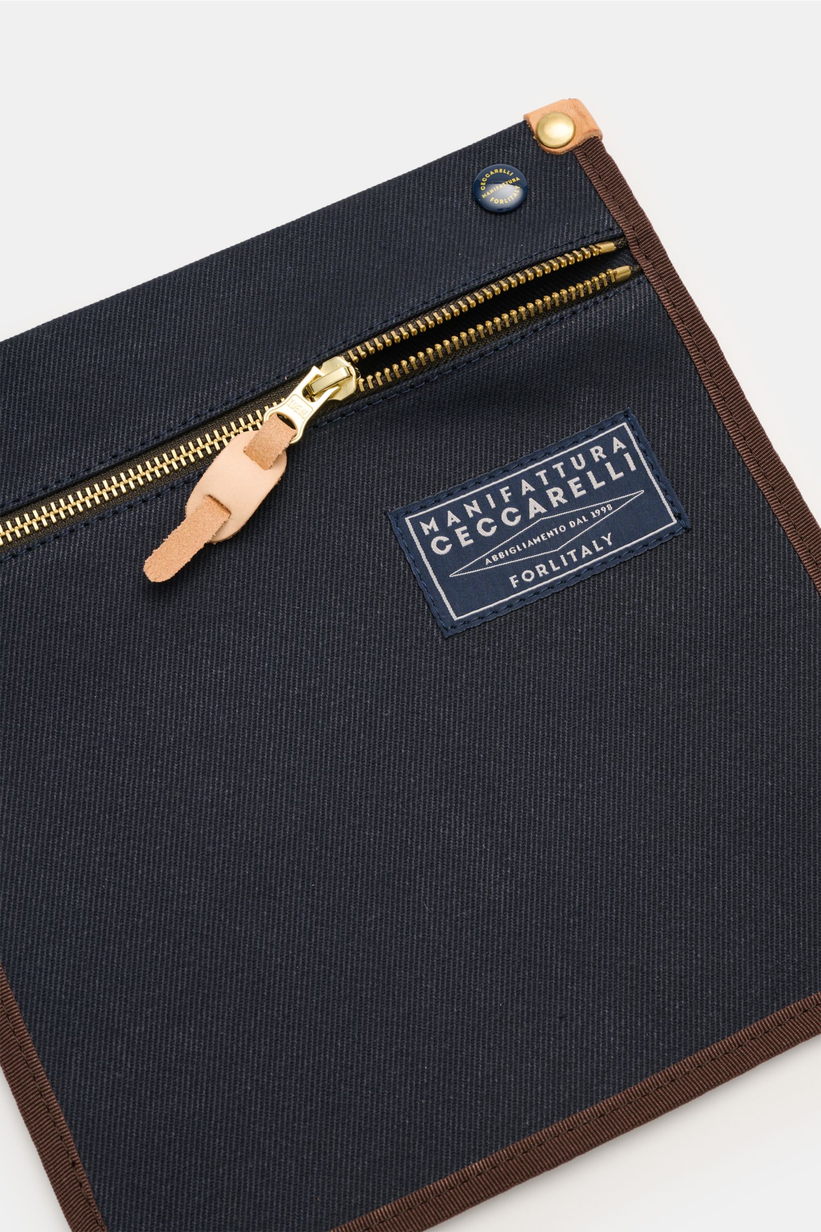 Nahaufnahme des Manifattura Ceccarelli Rucksack 'Laptop' navy aus reiner Baumwolle mit goldfarbenem Reißverschluss, Logo-Patch und braunen Kanten, frontal fotografiert.