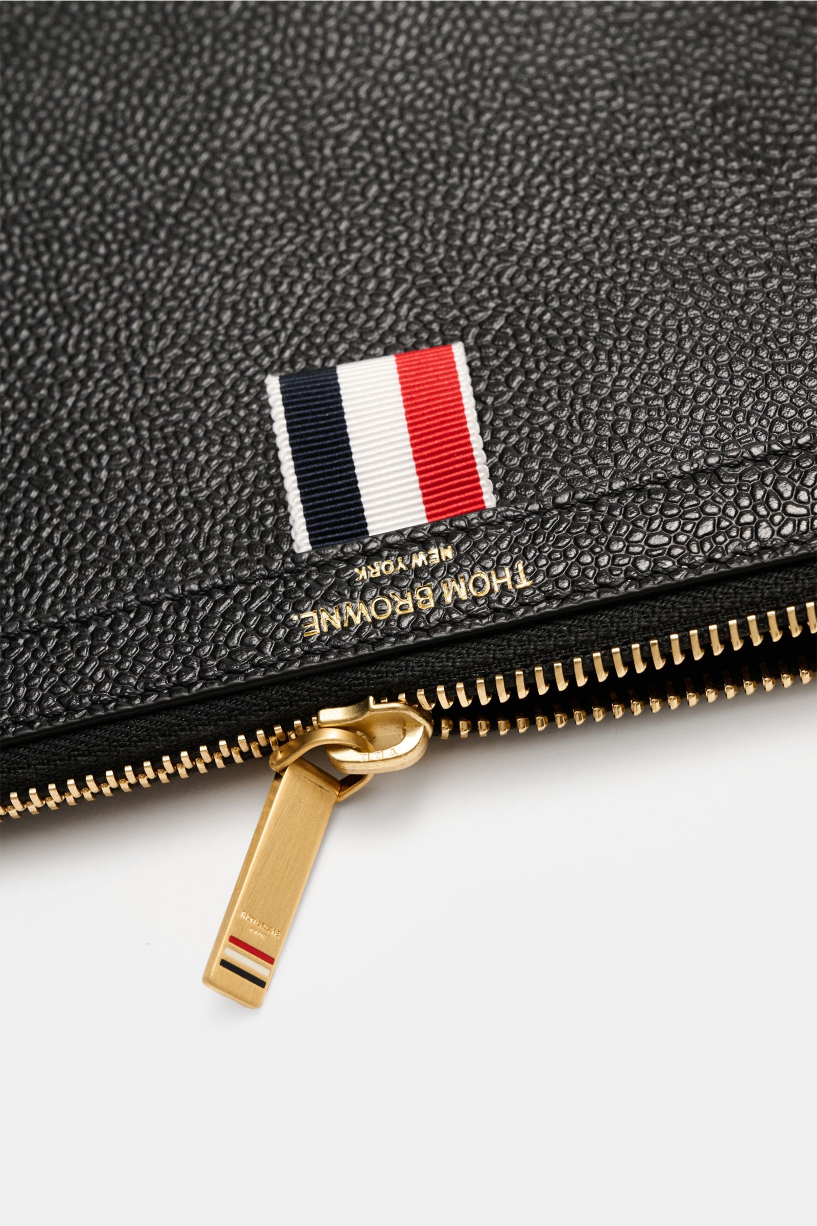 Alt tag (125 characters max):
Close-up top view of Thom Browne Dokumentenmappe schwarz with pebbled black leather, tricolor grosgrain, and gold zipper pull.

Description:
Die Dokumentenmappe aus edlem Leder von THOM BROWNE wird mit dem markentypischen 