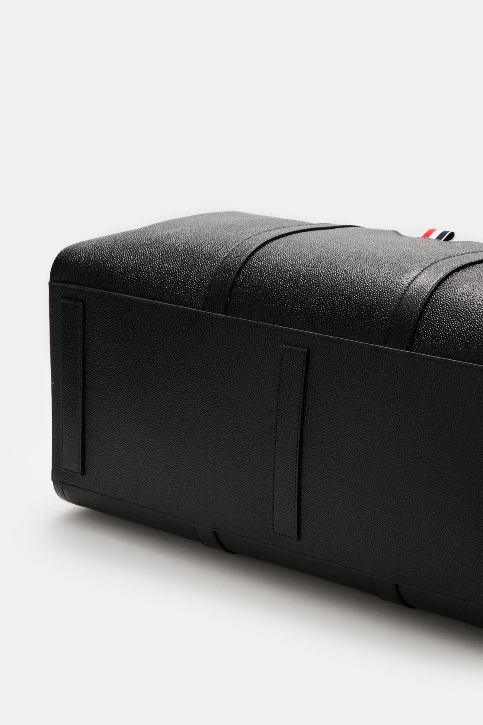 Thom Browne Weekender schwarz aus genarbtem Leder, Detailaufnahme von unten mit robusten Griffen und Tragegurt, goldfarbene Hardware.