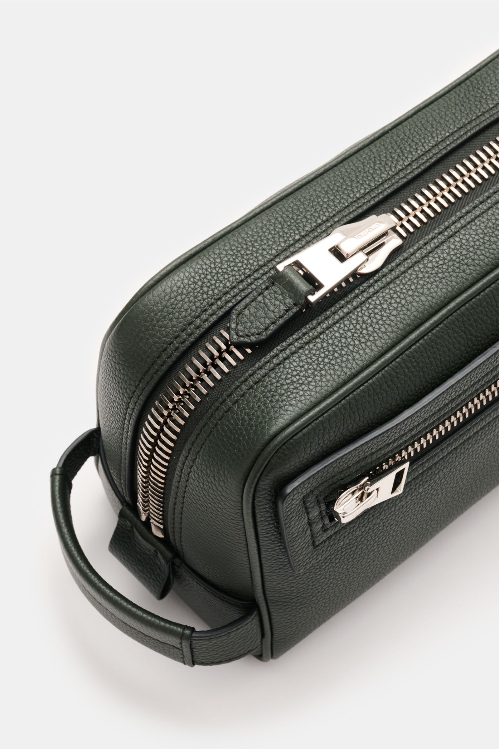 Close-up top-side view of Tom Ford Necessaire dunkelgrün in grained dark green calf leather with silver XL zipper hardware and handle, showing textured surface and zipper details. Dieses edle Necessaire von 