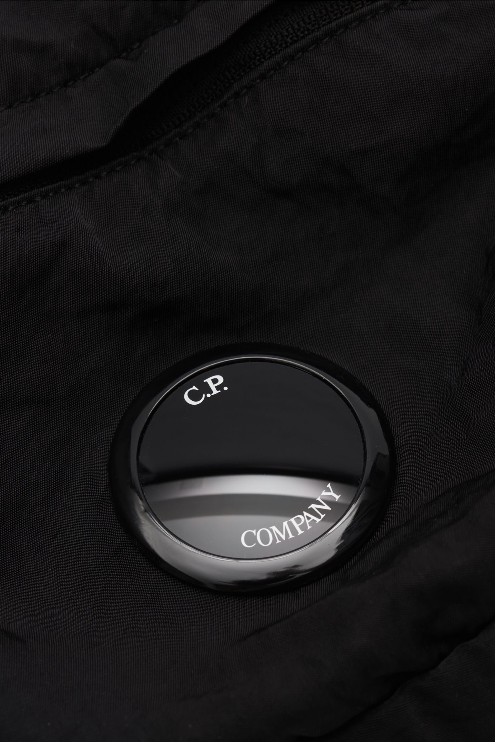 Close-up of the signature lens detail on the C.P. Company Belt bag black, photographed from above showing water repellent microfibre fabric. Don’t go on trips or into the city without this compact, piece-dyed belt bag made of water repellent microfibre by
