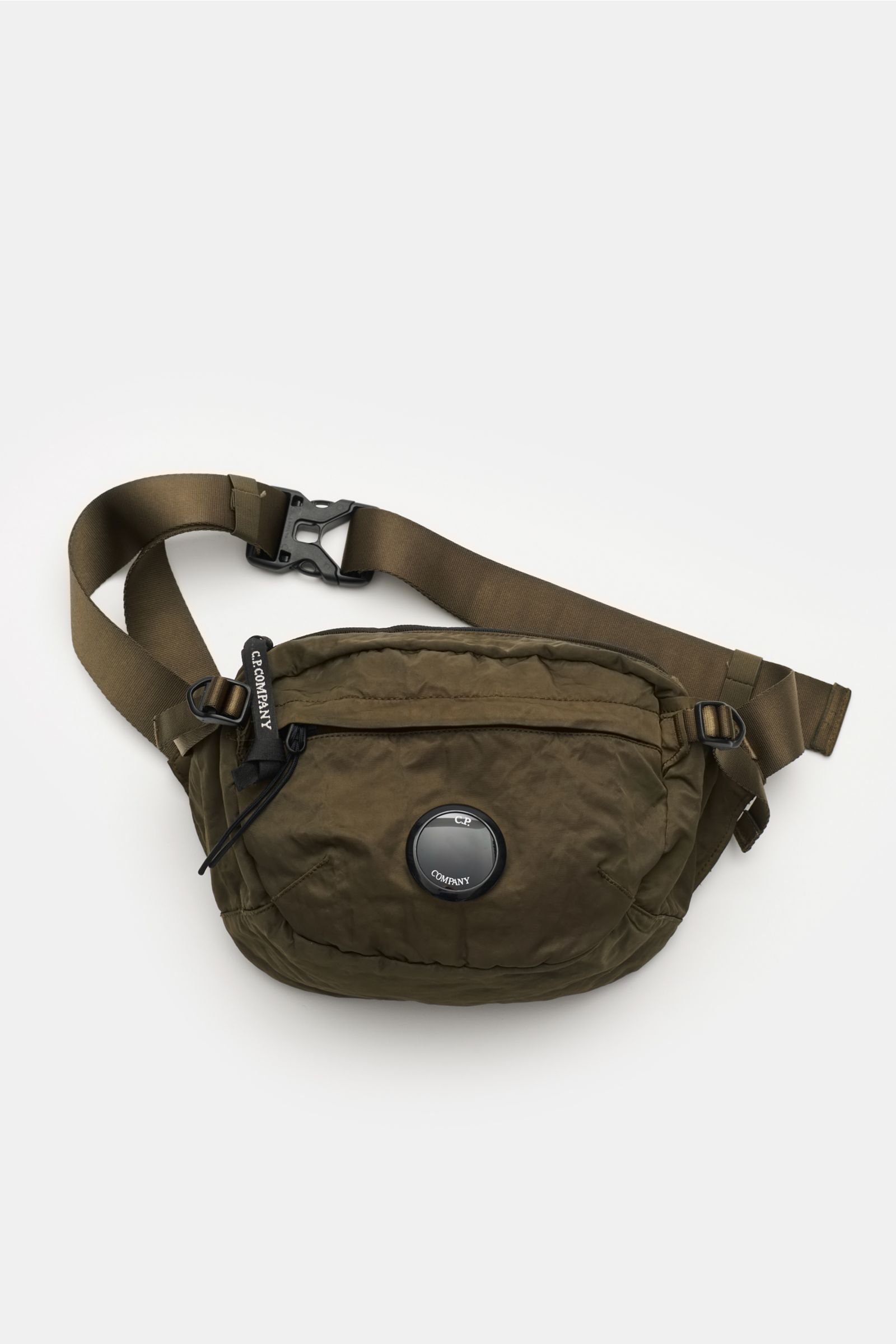 C.P. Company Belt bag olive shown from above, compact, piece-dyed, water repellent microfibre with adjustable belt, signature lens detail, padded back, and multiple zip compartments for flexible wear. Don’t go on trips or into the city without this compac
