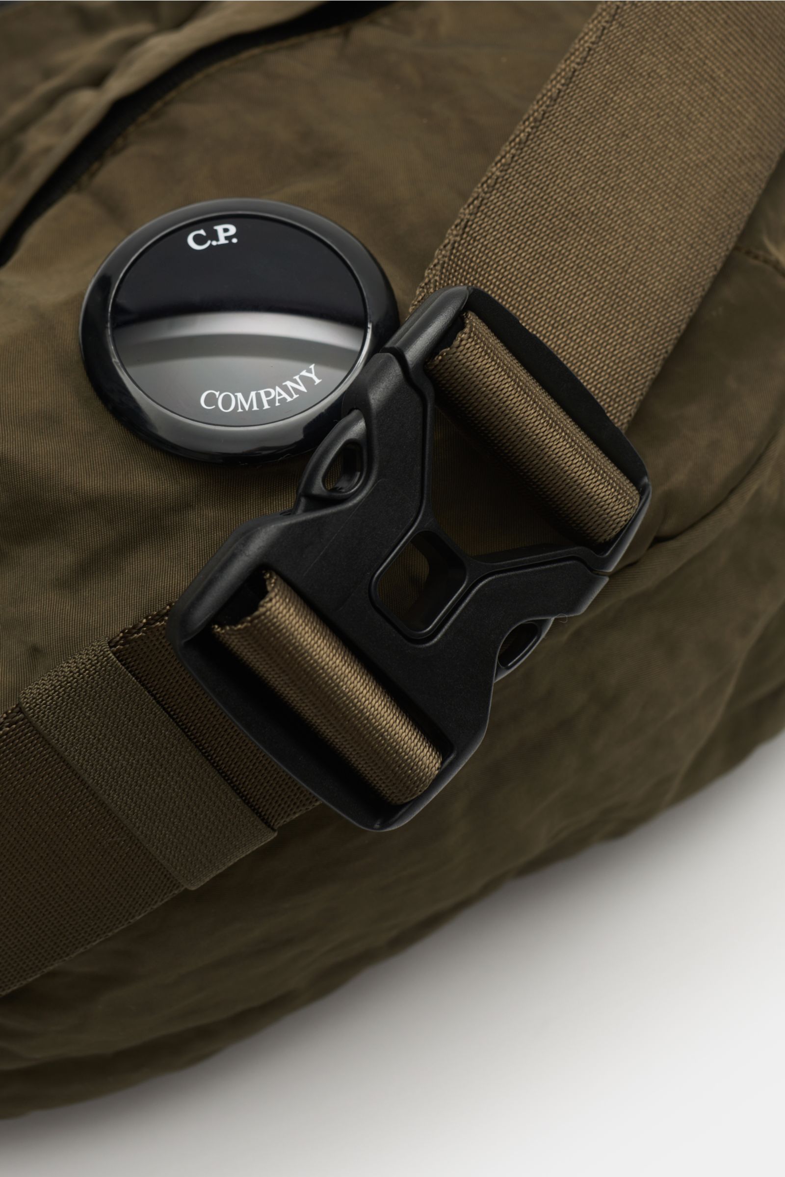 Close-up top view of the C.P. Company Belt bag olive showing water repellent microfibre, adjustable strap with black buckle, and signature lens detail. 

Don’t go on trips or into the city without this compact, piece-dyed belt bag made of water repelle