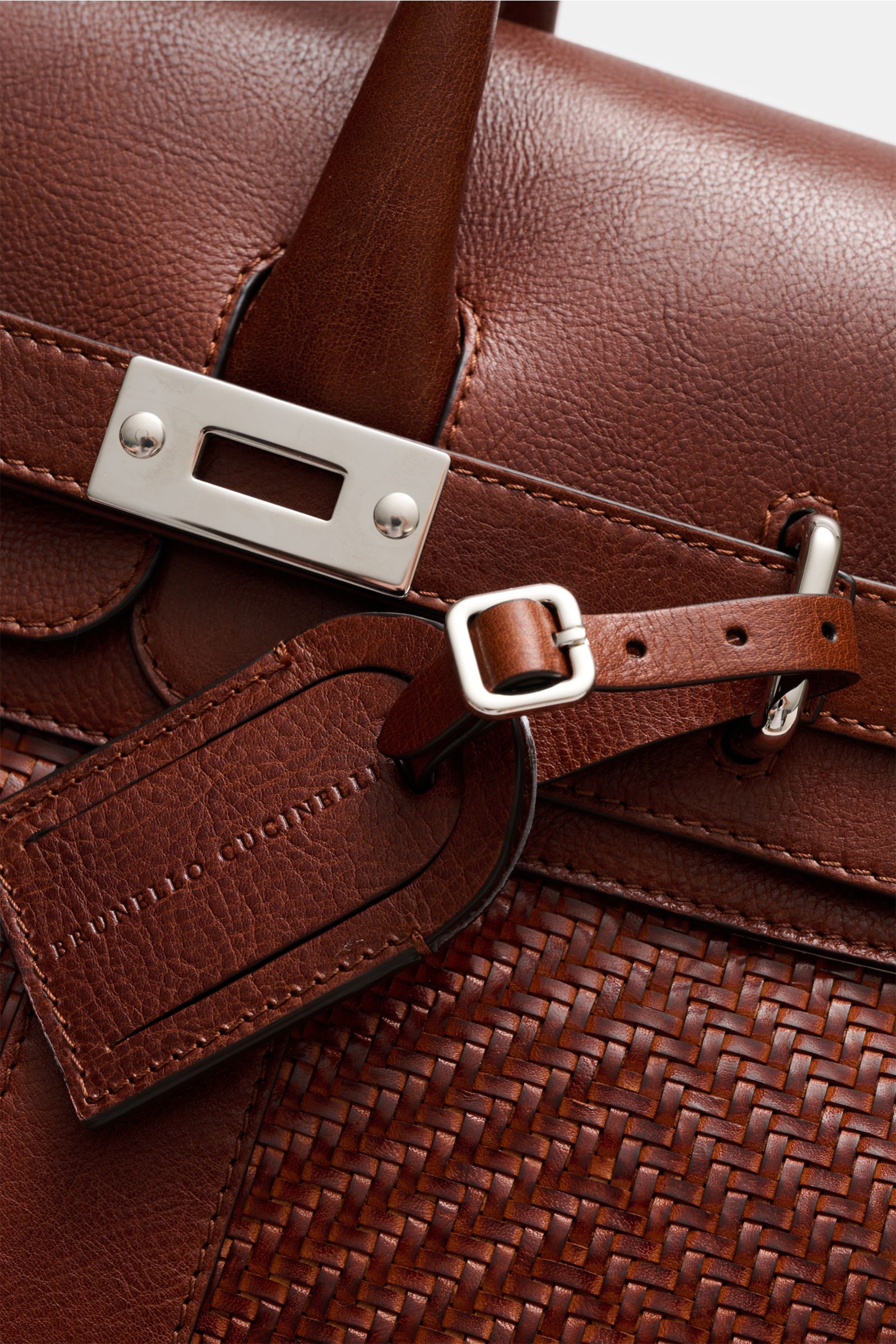 Close-up view of the Brunello Cucinelli Weekender bordeaux, showing textured grain leather, gold hardware, adjustable buckle, and leather address tag. A practical accessory with a spacious main compartment, interior zip pocket, slip pocket, water-repellen