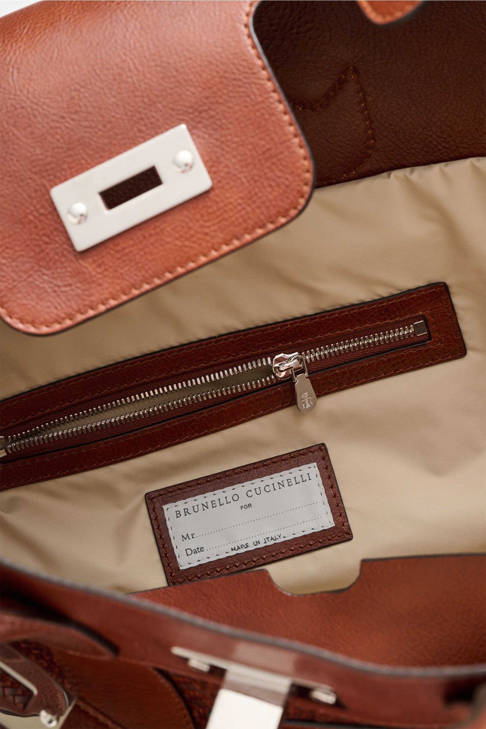 Close-up interior view of Brunello Cucinelli Weekender bordeaux showing beige water-repellent lining, zippered pocket, leather trim, and label.