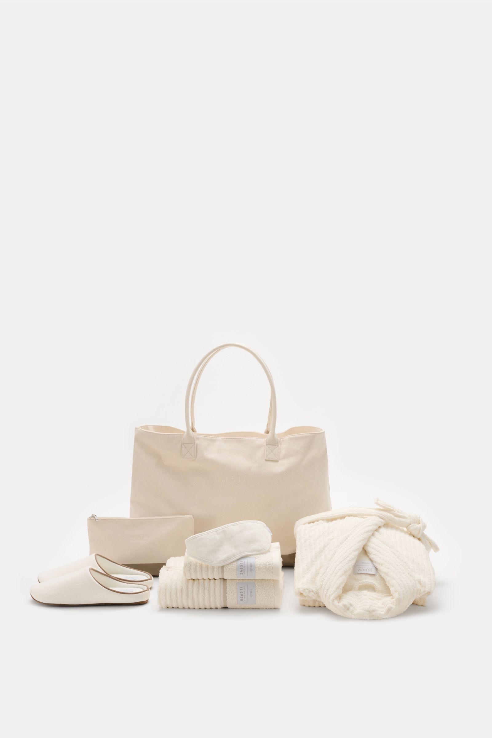 Front view of 04651/ A trip in a bag Reise-Set 'Voyage' creme/weiß featuring a large cream canvas shopper with sturdy handles, a folded bathrobe, hand towel, bath towel, zippered necessaire, indoor slippers, and a sleep mask, all neatly arranged for a sty