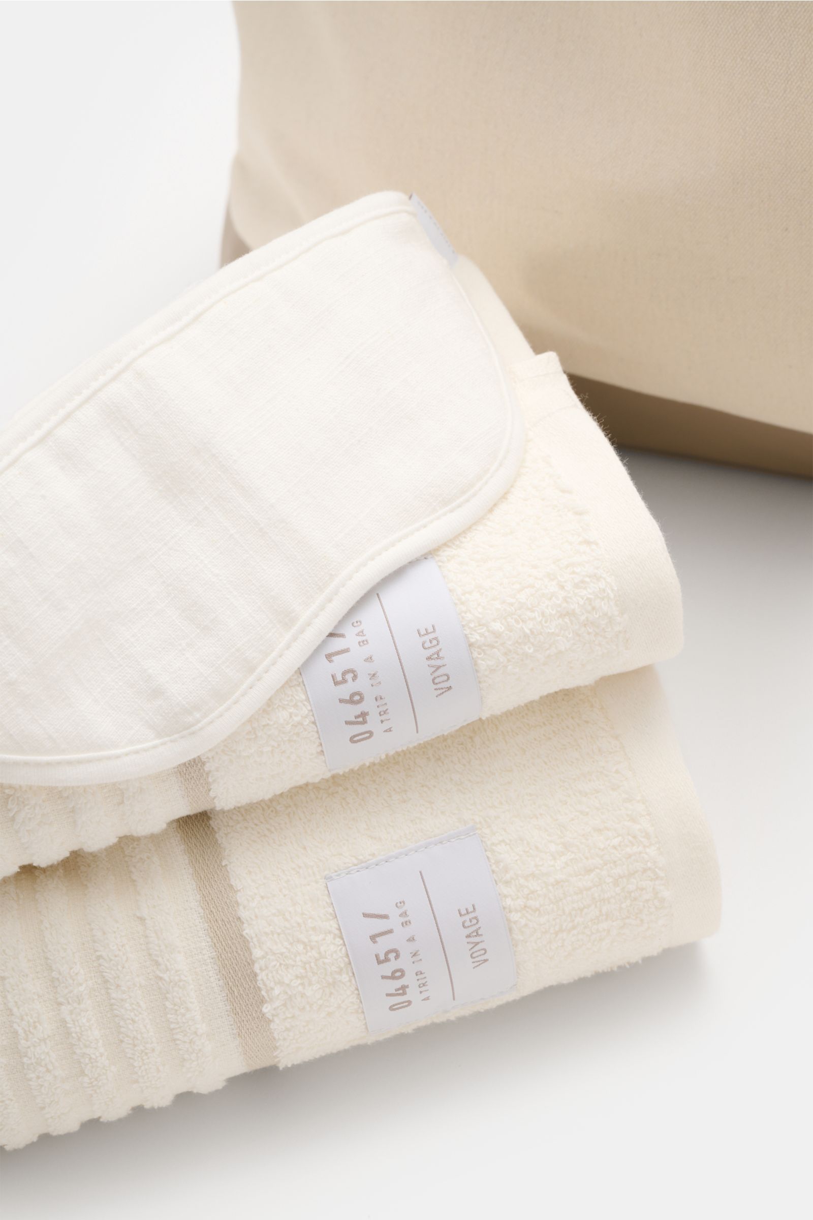 Close-up from above of cream and white towels with 04651/ A trip in a bag labels, part of the 04651/ A trip in a bag Reise-Set 'Voyage' creme/weiß travel set.

Description: A thoughtfully curated travel essential, the 04651/ A trip in a bag Reise-Set 'Voy