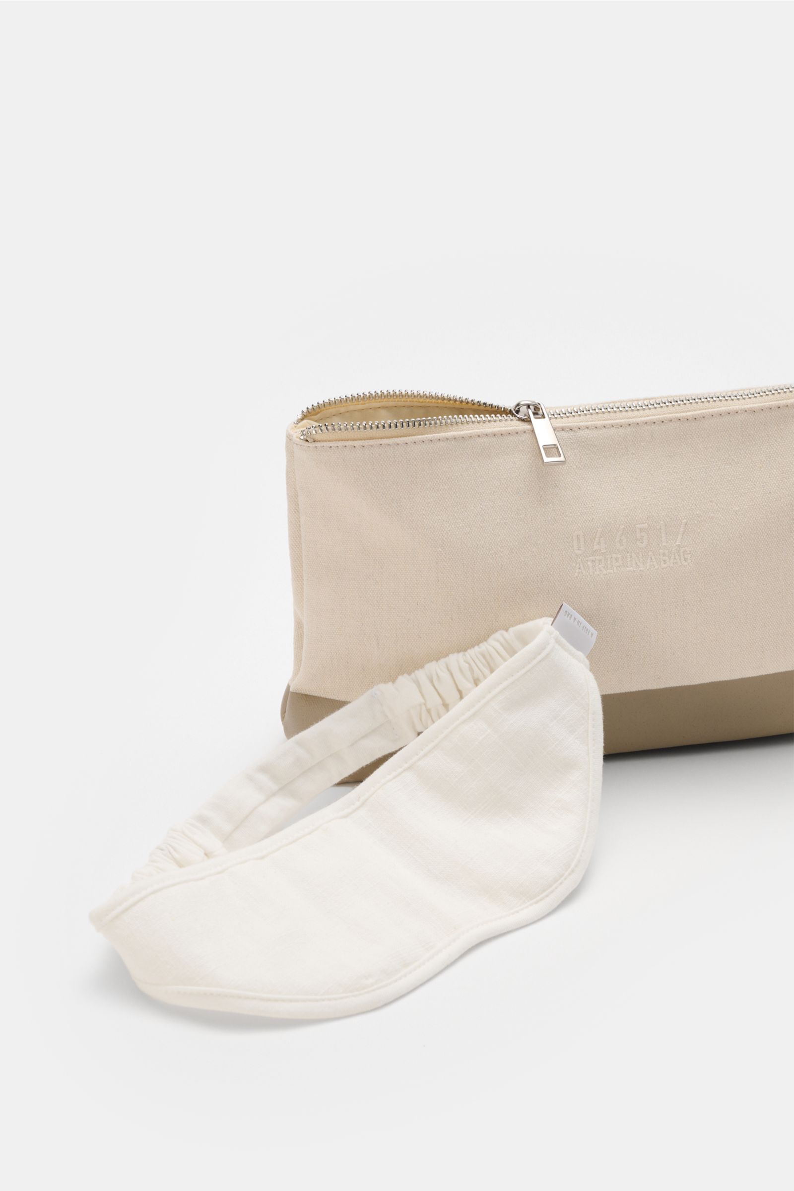 Front angled view of the 04651/ A trip in a bag Reise-Set 'Voyage' creme/weiß showing a cream canvas zippered pouch and a folded white sleep mask, part of a travel-essential set including a canvas shopper, bathrobe, towels, necessaire, slippers, all styli