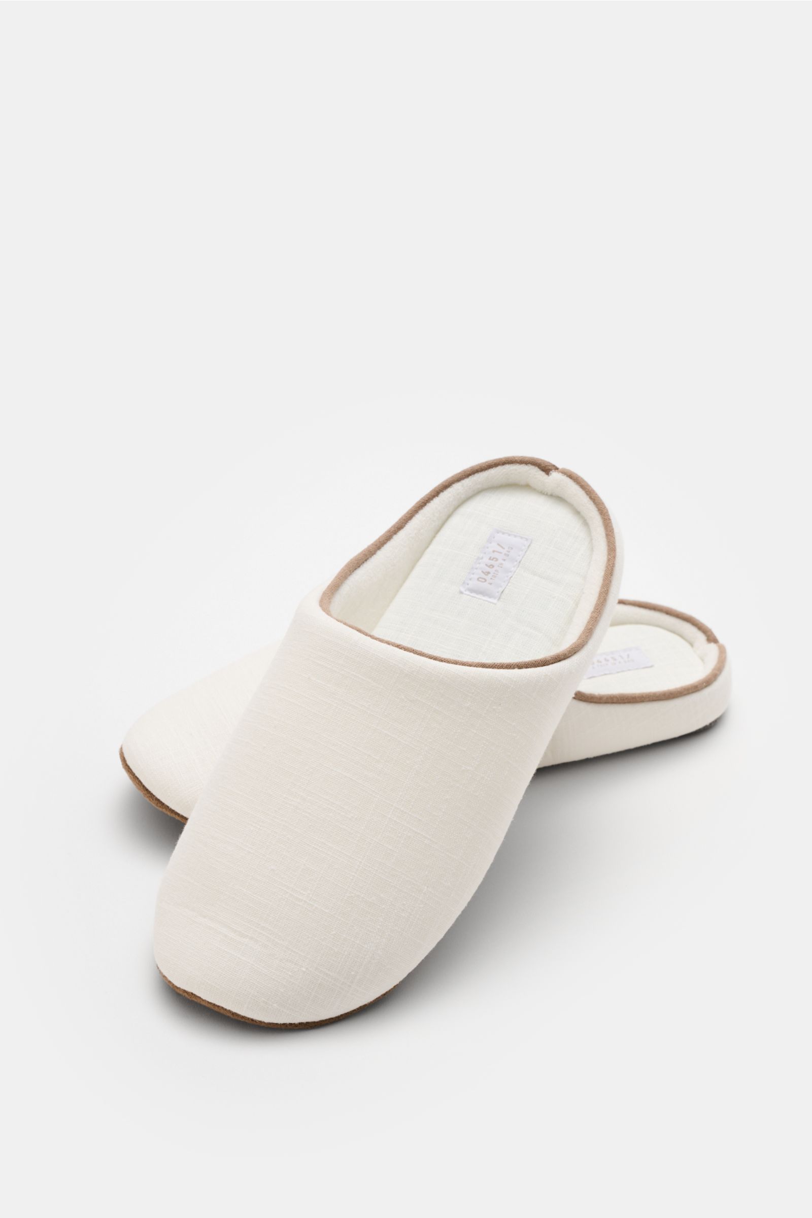 Front-side view of beige indoor slippers with brown trim from the 04651/ A trip in a bag Reise-Set 'Voyage' creme/weiß travel set, part of a stylish canvas shopper bundle with bathrobe, towels, necessaire, slippers, and sleep mask for relaxed hotel or hol