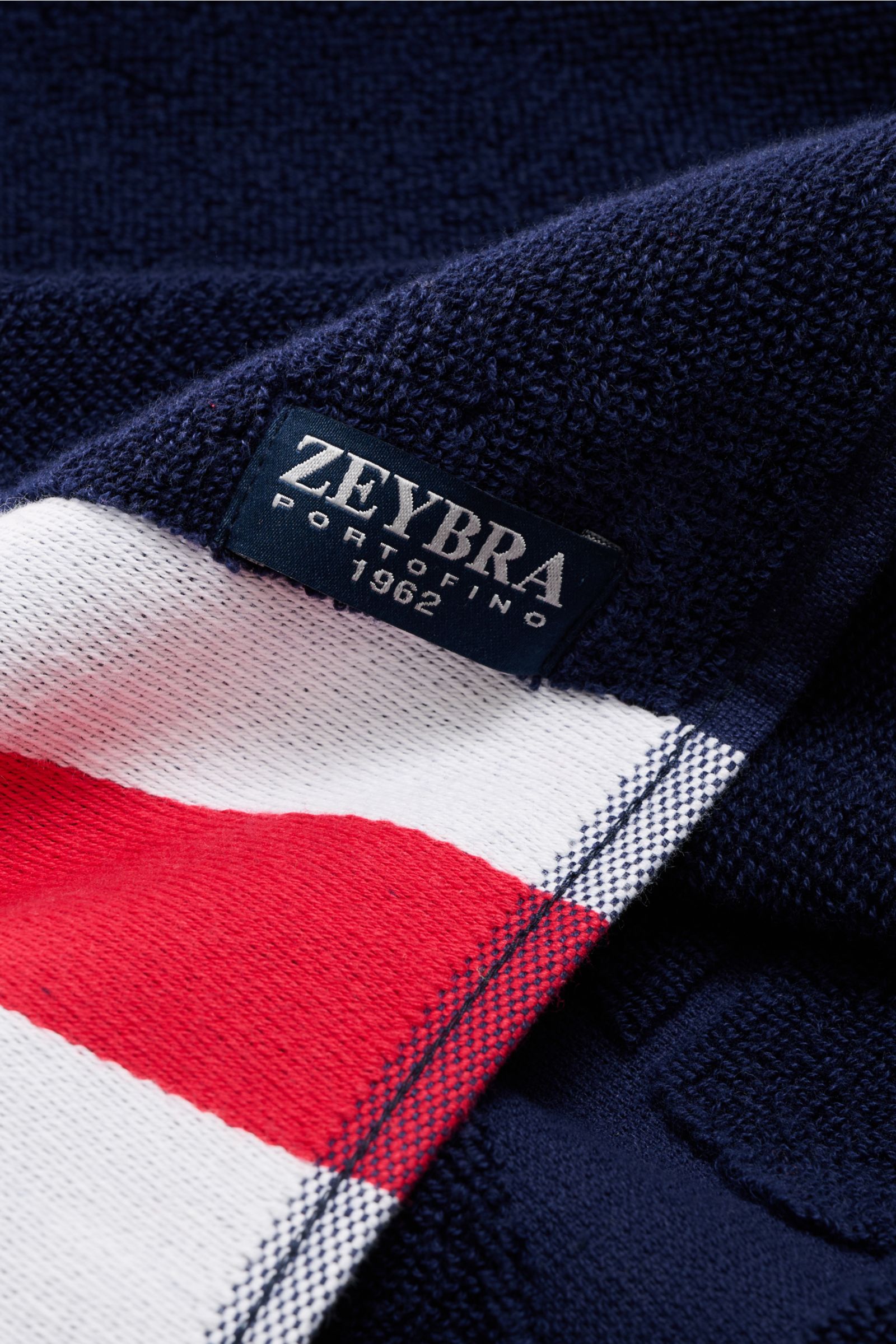 Close-up view of the navy blue Zeybra Portofino 1962 Frottee-Strandtuch with a tricolor border and woven tonal logo tag, showing texture and stitching.

Ausgiebig Sonnenbaden mit ZEYBRA PORTOFINO 1962: Dieses edle Frottee-Tuch bietet genügend Platz zum