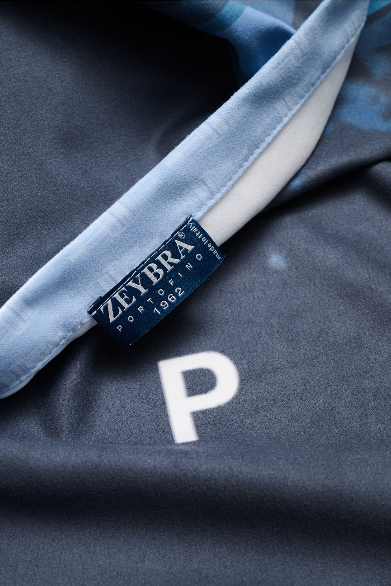 Nahaufnahme aus schräger Perspektive des Zeybra Portofino 1962 Strandtuchs graublau gemustert mit weichem Microfaserstoff und Label.