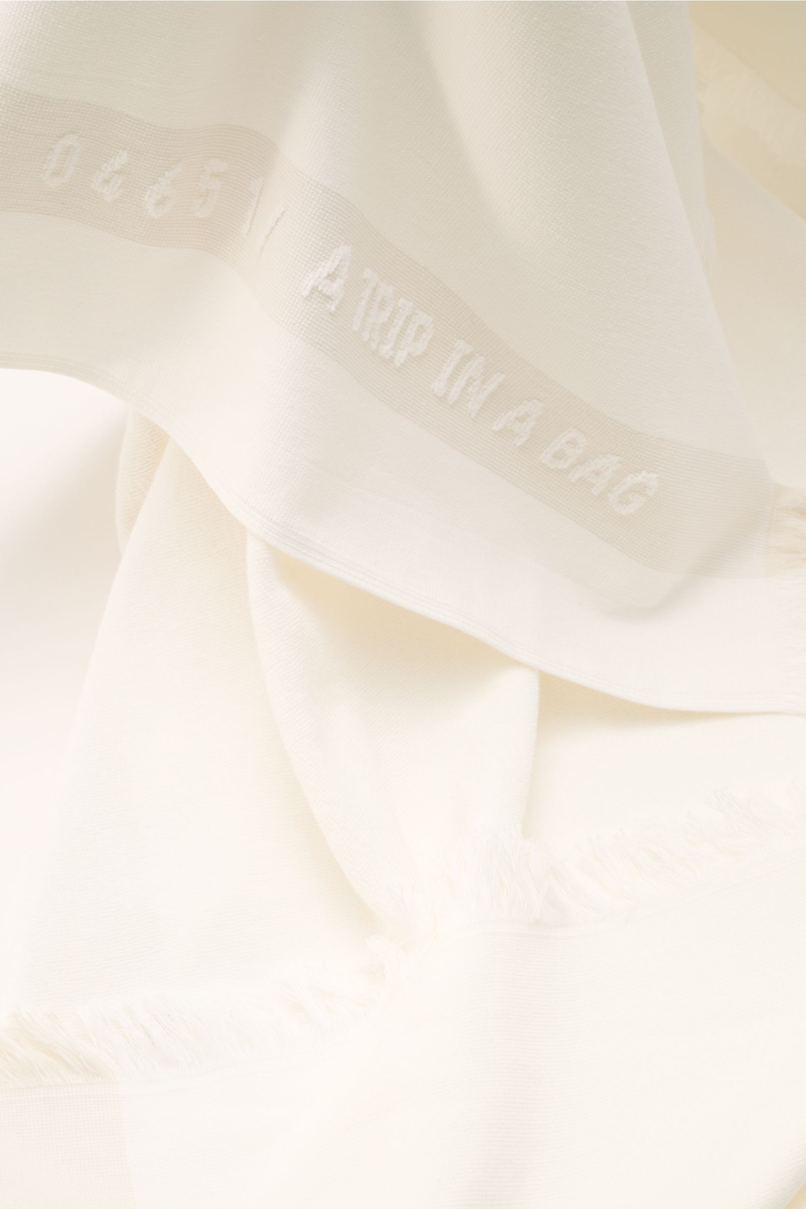 Offwhite 04651/ A trip in a bag Strandtuch shown from a close-up top perspective, made of pure cotton soft terry with narrow fringe edges, approx. 95x175 cm. Elegantes Strand-Accessoire: Das Strandtuch aus reinem Baumwoll-Frottée von 04651/ A TRIP IN A BA