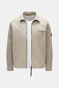 Front view of C.P. Company Overshirt sand, a slim fit, lightweight pure cotton layering piece with two-way zipper, flap chest pocket, collar, sleeve logo pocket, and cuffed sleeves. Lässiges Layering-Piece: Das Overshirt von C.P. COMPANY ist der ideale Be