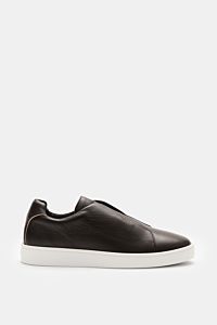 Side view of Aurélien Slip-on-Sneaker dunkelbraun in finely grained dark brown leather with round toe, elastic bands, padded collar, subtle logo, leather lining, and flexible white rubber sole, showcasing minimalist design and craftsmanship.