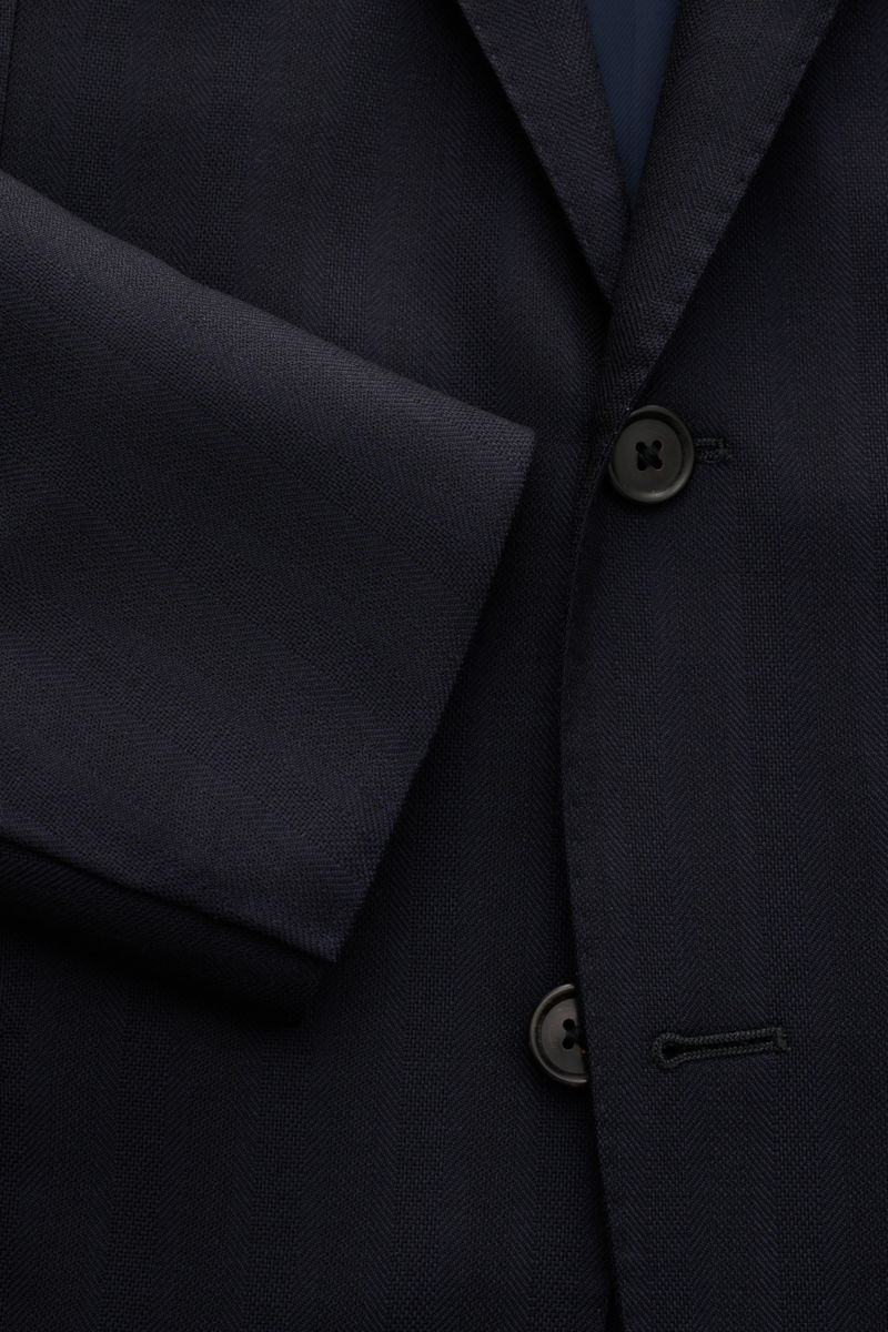 Corneliani Anzug dark navy aus reiner Schurwolle, Slim Fit, tonaler Fischgrat, frontale Nahaufnahme von Sakko mit Zwei-Knopf-Stil und fallendem Revers.