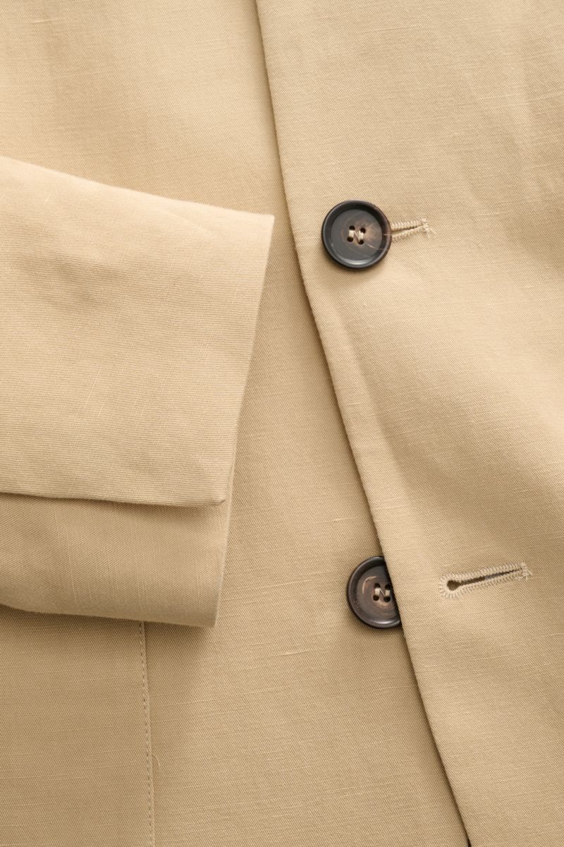 Close-up front view of Doppiaa Anzug 'Aanetoant' beige jacket showing smooth Lyocell-linen fabric, soft texture, five-button style, variable collar, and concealed sleeve buttons, highlighting its unconstructed design and comfortable summer tailoring.
