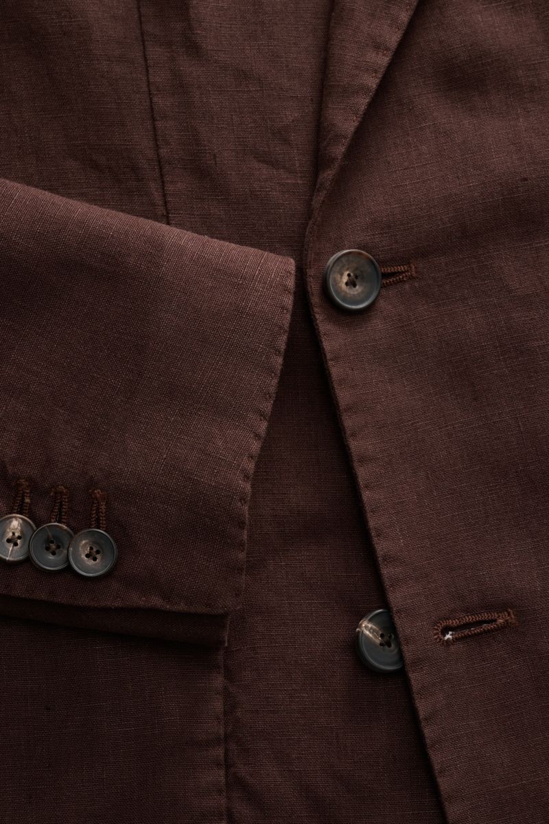 Nahaufnahme des braunen Santaniello Anzugs aus reinem Leinen, die taillierte Knopfleiste und Ärmel mit Kissing Buttons zeigt, vintage-inspirierter Slim Fit, fotografiert aus leicht seitlicher Frontperspektive.