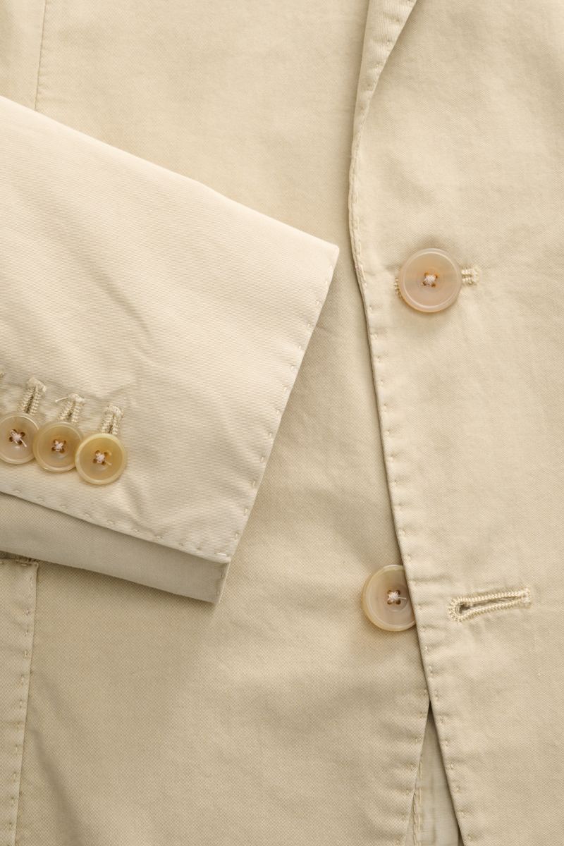 Close-up top-down view of the Santaniello Anzug sand jacket sleeve and front button area, showcasing fine cotton twill fabric and buttons. Lässige Eleganz mit Stil: Dieser Anzug von SANTANIELLO überzeugt mit feinstem Baumwoll-Twill und modernem Design - i