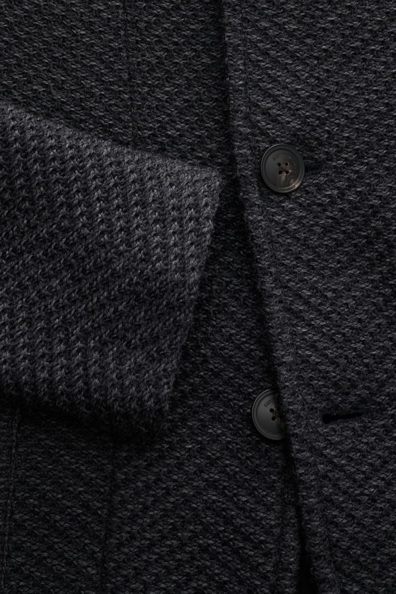 Close-up front view of the Emporio Armani Blazer dunkelgrau meliert, showing its dark grey melange wool fabric with airy herringbone texture, five-button style, variable lapel, patch hip pockets, slim fit, and unconstructed design. Markant, leicht, stilvo