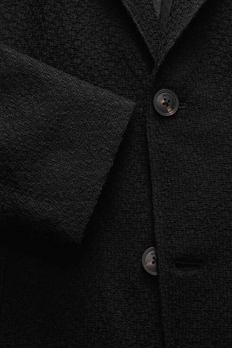Close-up front view of Emporio Armani Strickblazer schwarz showing its fine, lightweight wool knit texture, two-button style, slim fit, and unconstructed design with patch hip pockets and notched lapel. Edles Piece mit Twist von GIORGIO ARMANI: Mit die