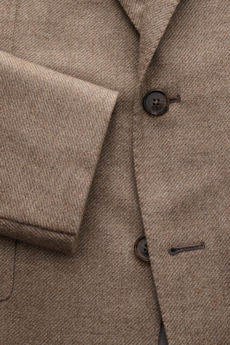 Nahaufnahme des Caruso Sakko 'Aida' beige meliert, Slim Fit mit weicher reiner Wolle, Zwei-Knopf-Stil, fallendem Revers, Brust- und Hüfttaschen, unfertigen Ärmelabschlüssen, Seitenschlitzen und geschmeidigem Futter, aus schräger Perspektive fotografiert.