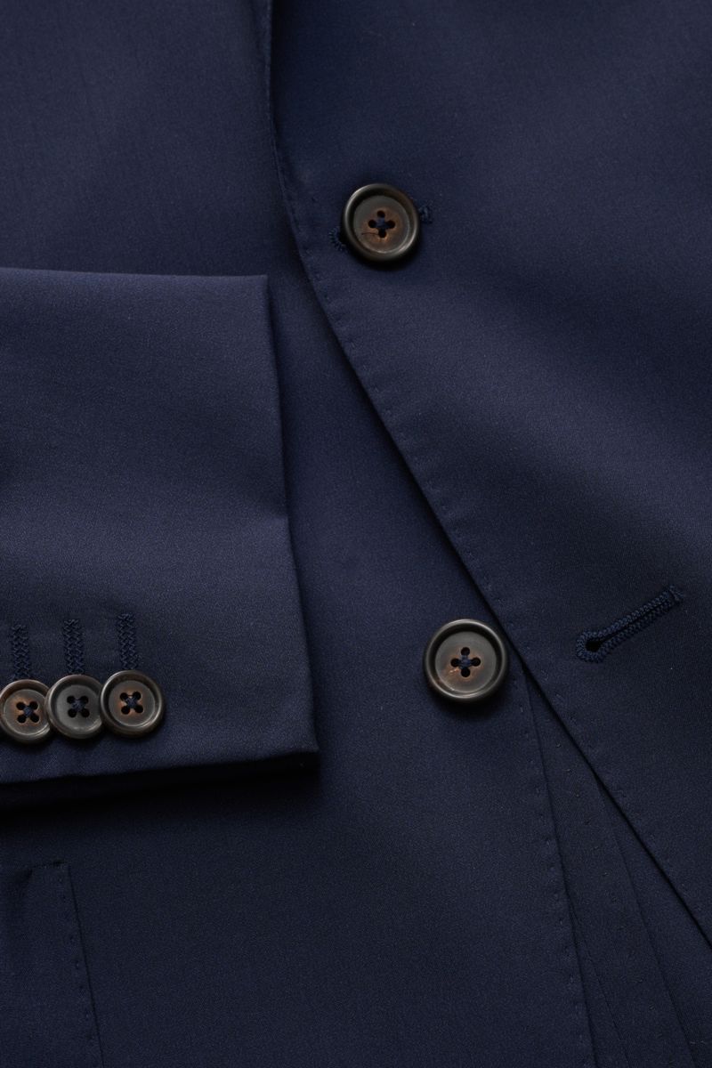 Nahaufnahme des Corneliani Sakko navy aus feinem Wolle-Seiden-Mix, Slim Fit, taillierter Zwei-Knopf-Stil, glatter Griff, Ärmel mit Knöpfen, fallendes Revers, fotografiert von schräger Draufsicht.