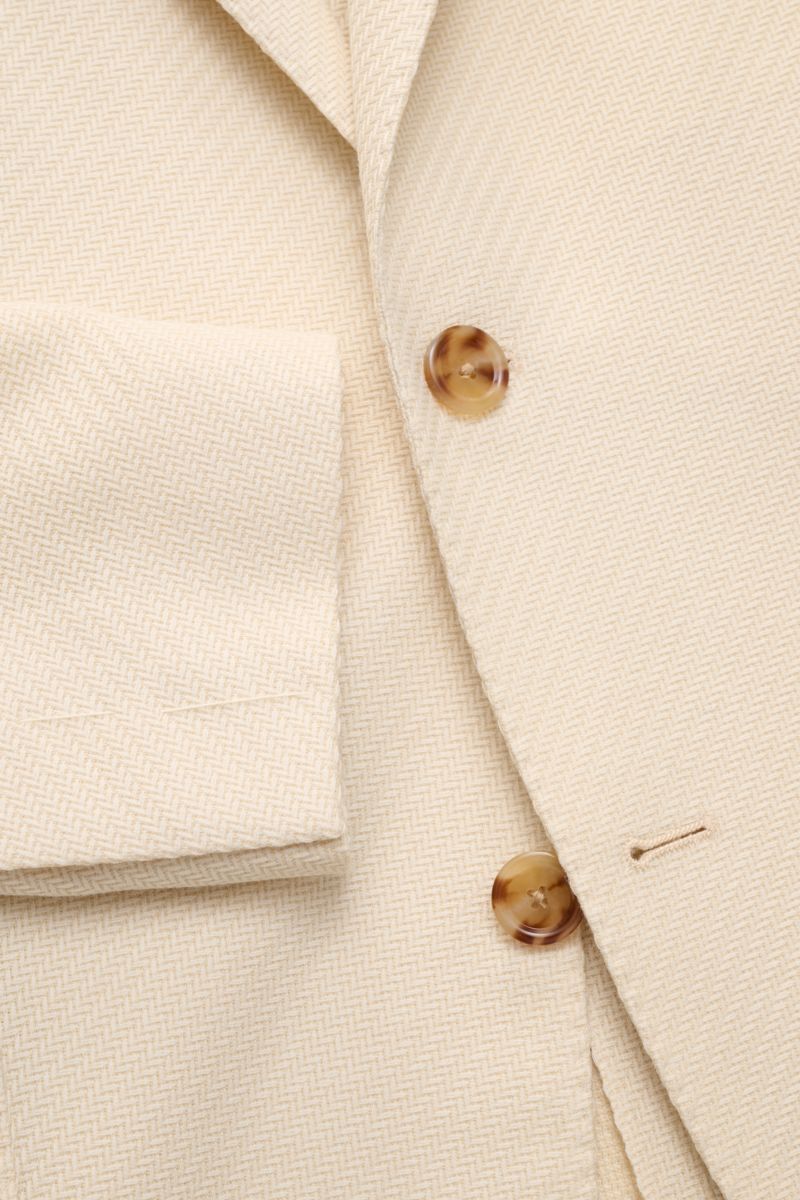 Close-up front view of Lardini Smart-casual jacket cream showing tonal herringbone pattern, two tortoiseshell buttons, step lapel with flower pin, and cuff detail. 

An Italian design classic: This smart-casual jacket from LARDINI made of wool and cott